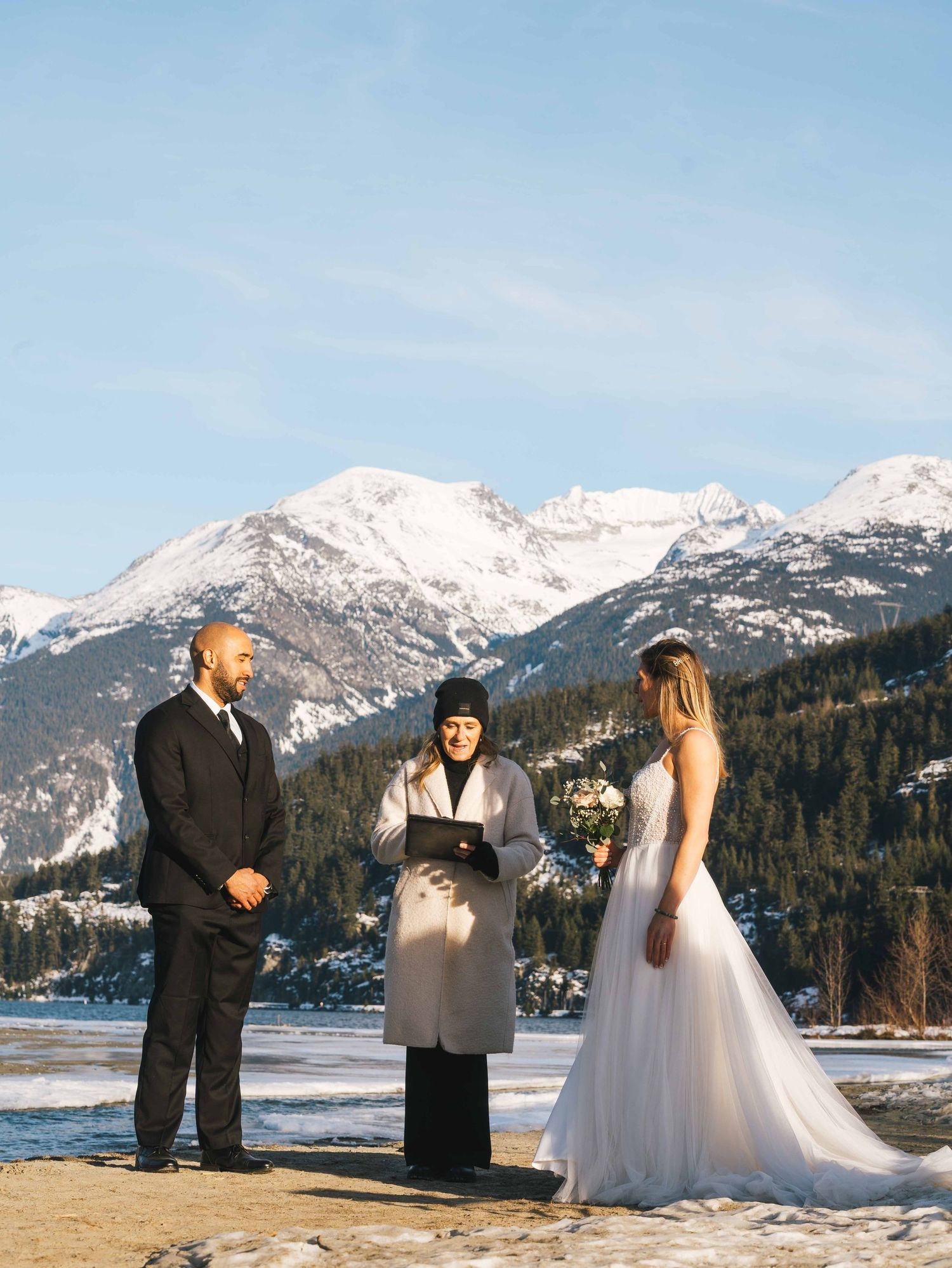 Couple exchanging vows at a stunning winter elopement ceremony with snow-capped mountains backdrop.