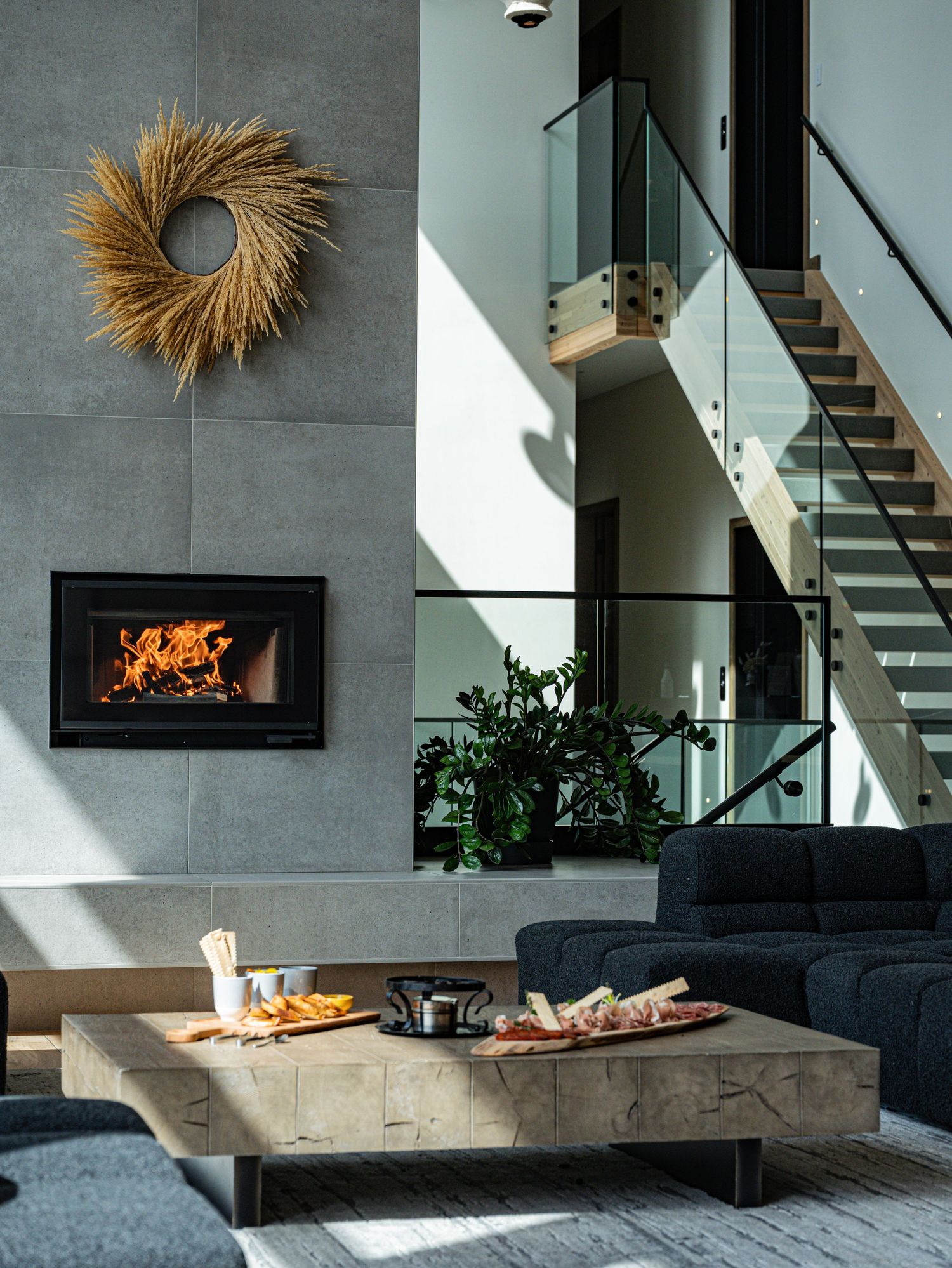 Contemporary living room with fireplace, staircase, sofa and charcuterie board on coffee table.
