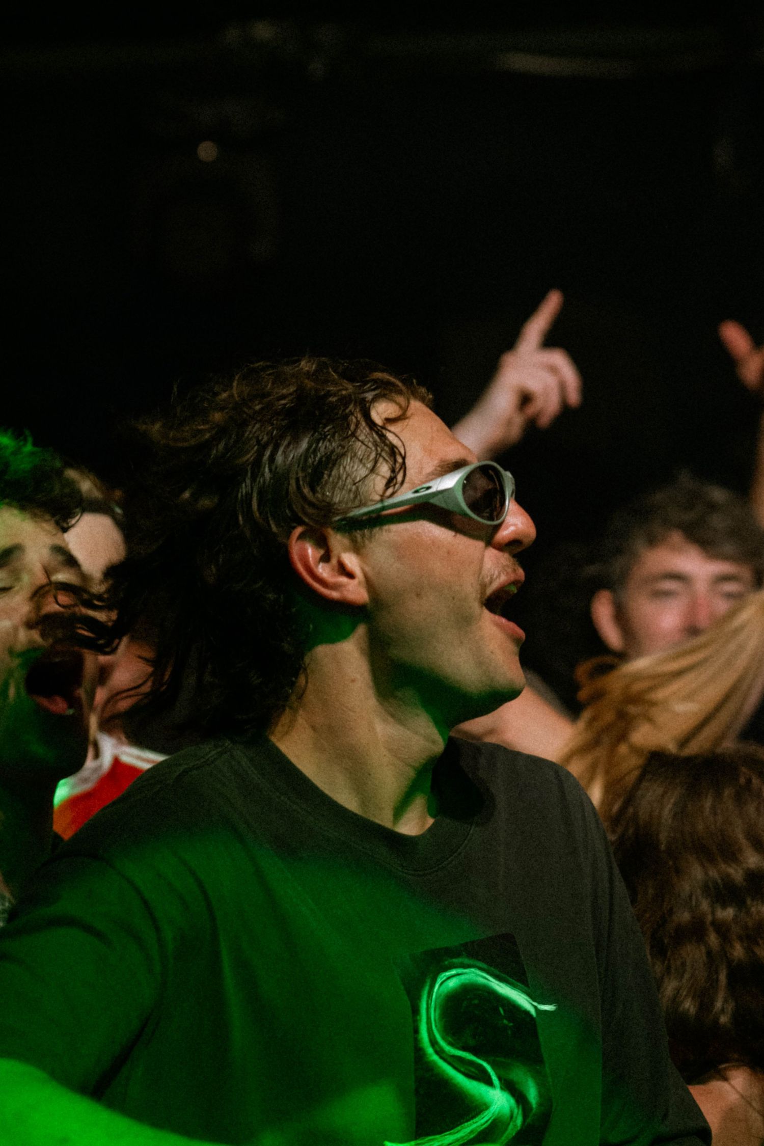 Excited concert-goer in silver glasses singing under green stage lights in a dark venue.