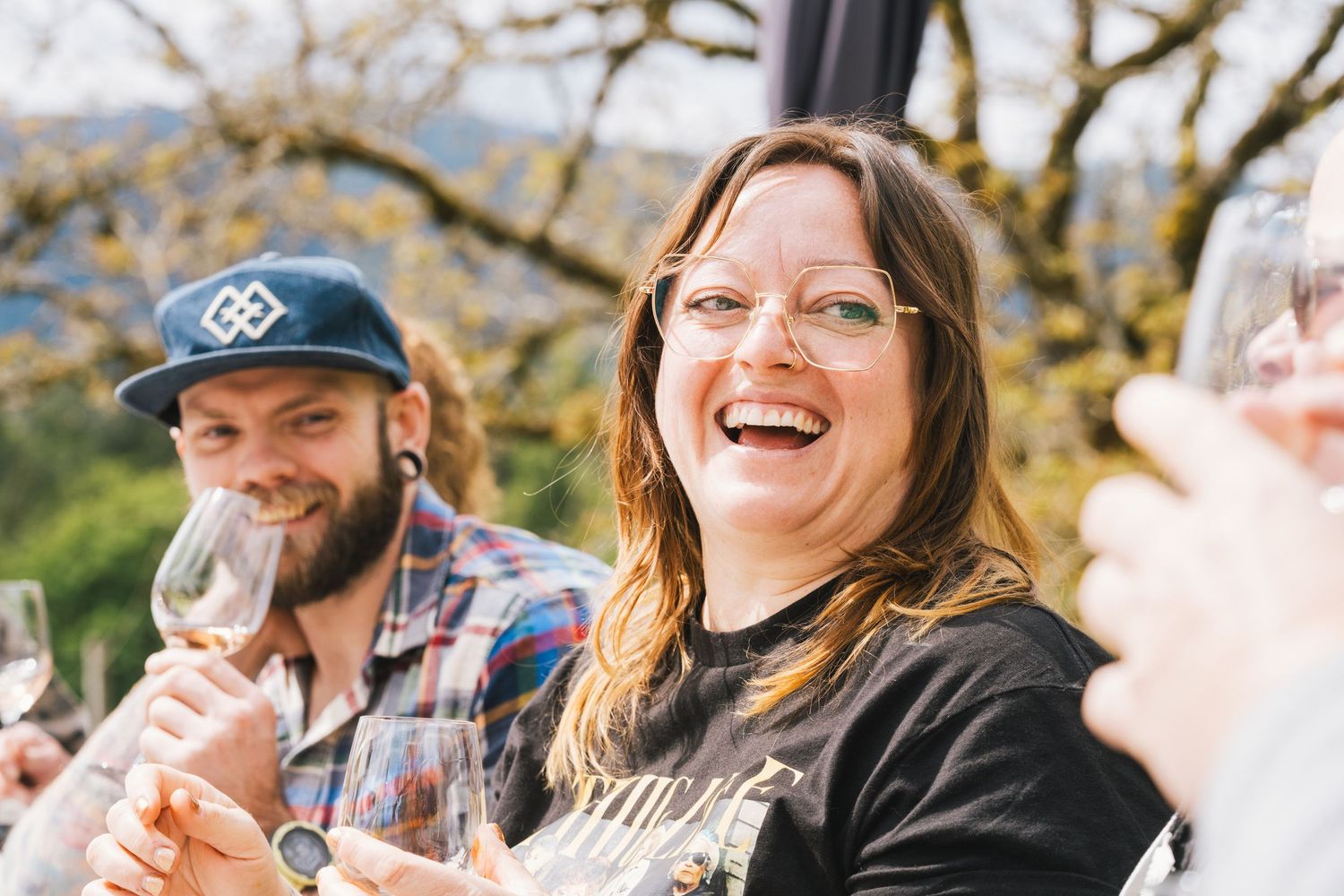 Happy woman laughing and holding a wine glass at an outdoor wine tasting event with friends.