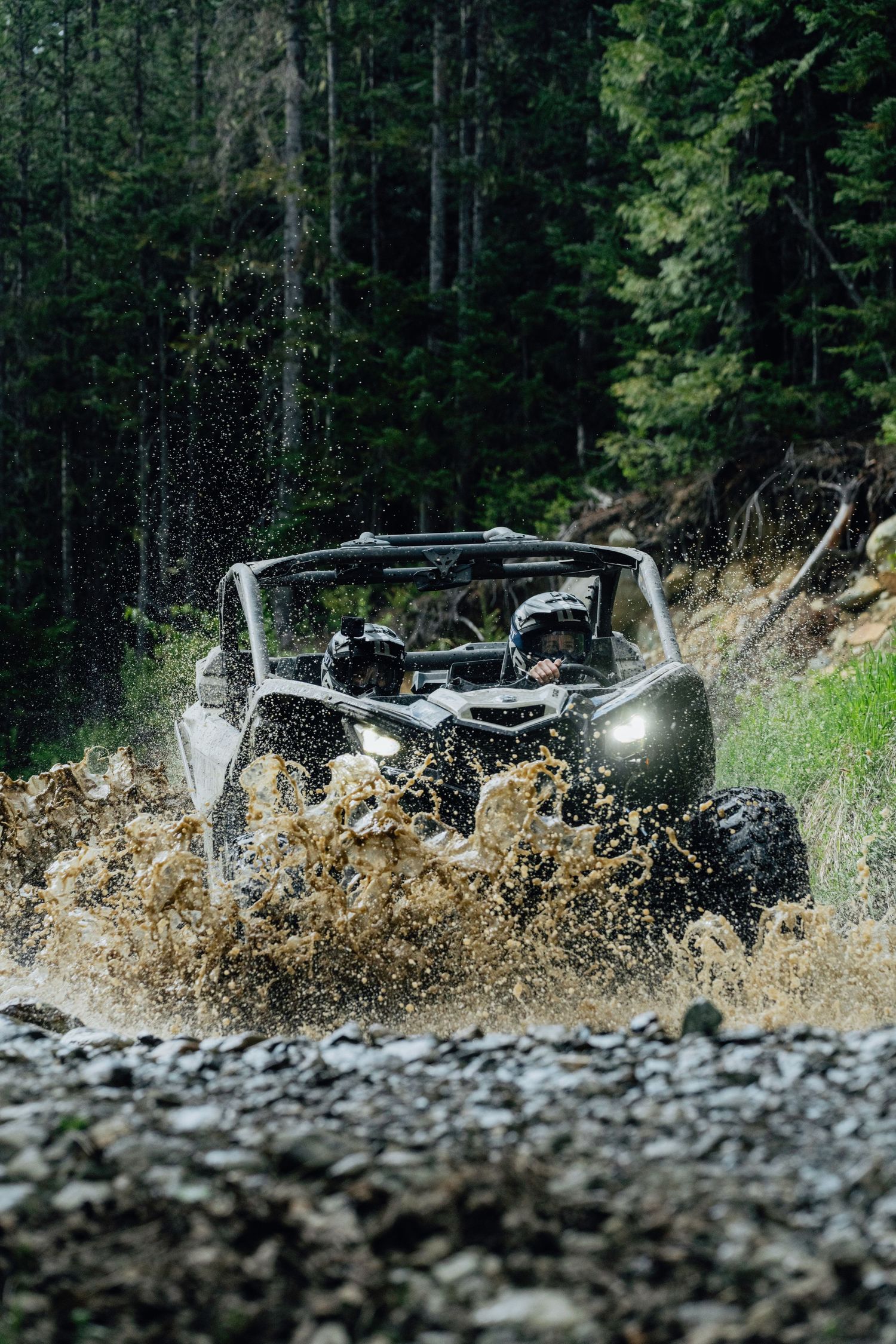 Off-road UTV splashing through muddy terrain in a dense forest trail.