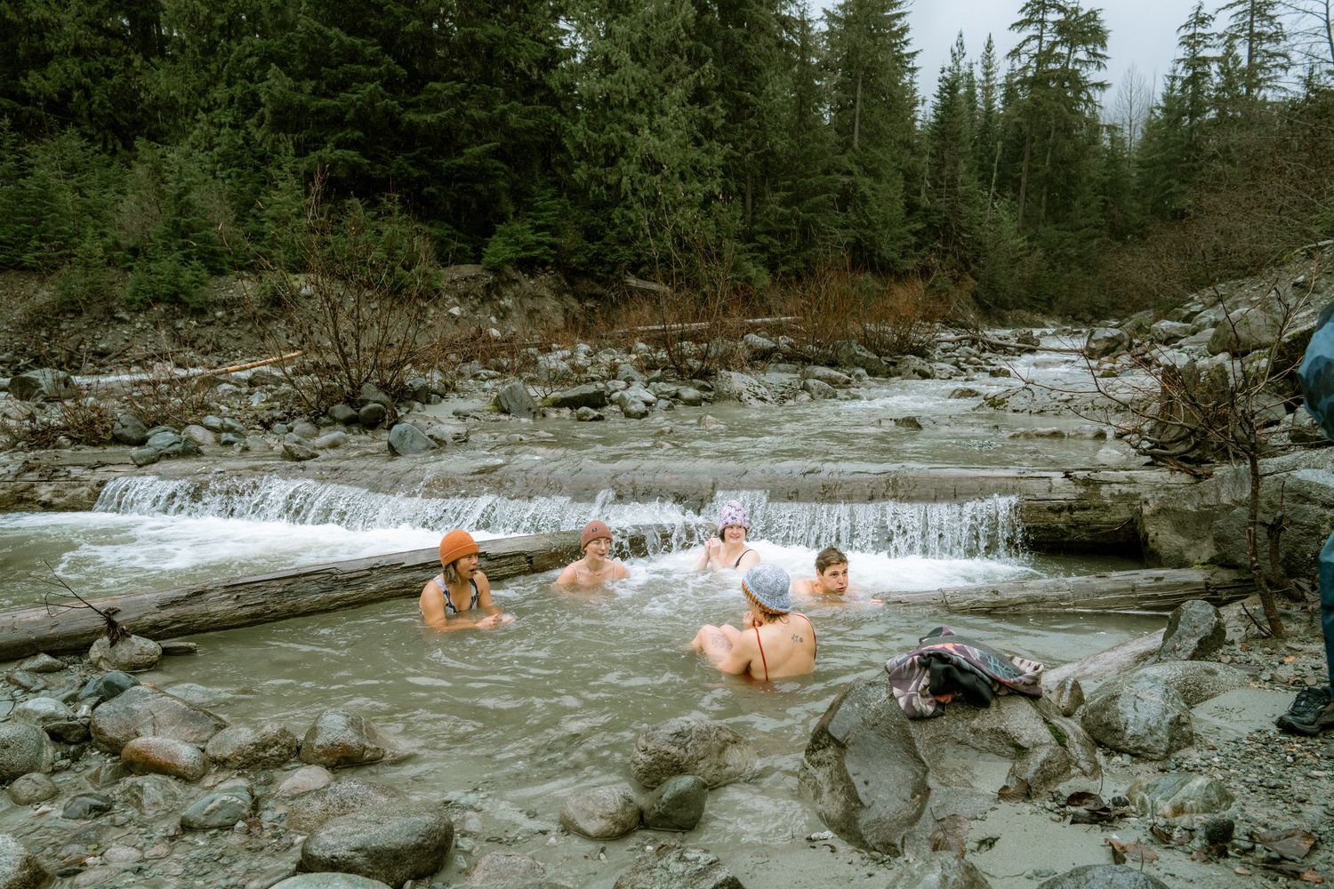 Group of friends relaxing in a rocky mountain river stream surrounded by evergreen forest.
