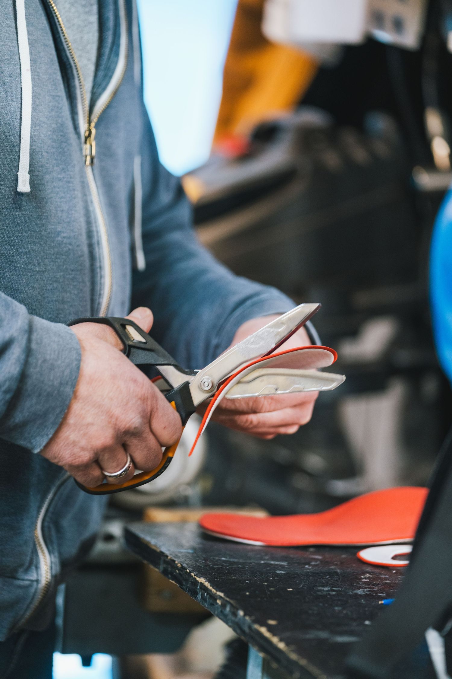 Craftsman cutting red shoe insole with large scissors in a workshop setting.