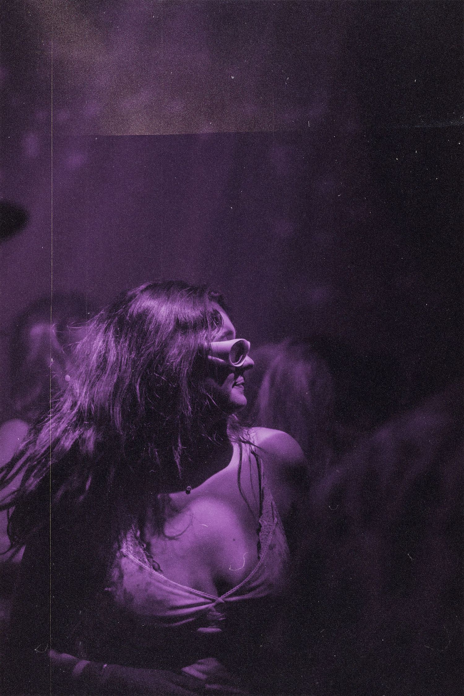 Woman with long hair and sunglasses dancing under purple neon lights at a nightclub.