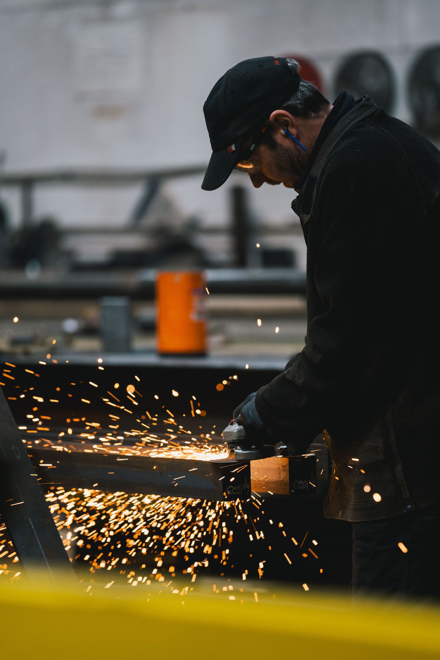 Industrial worker grinding metal with an angle grinder creating bright sparks in a workshop.