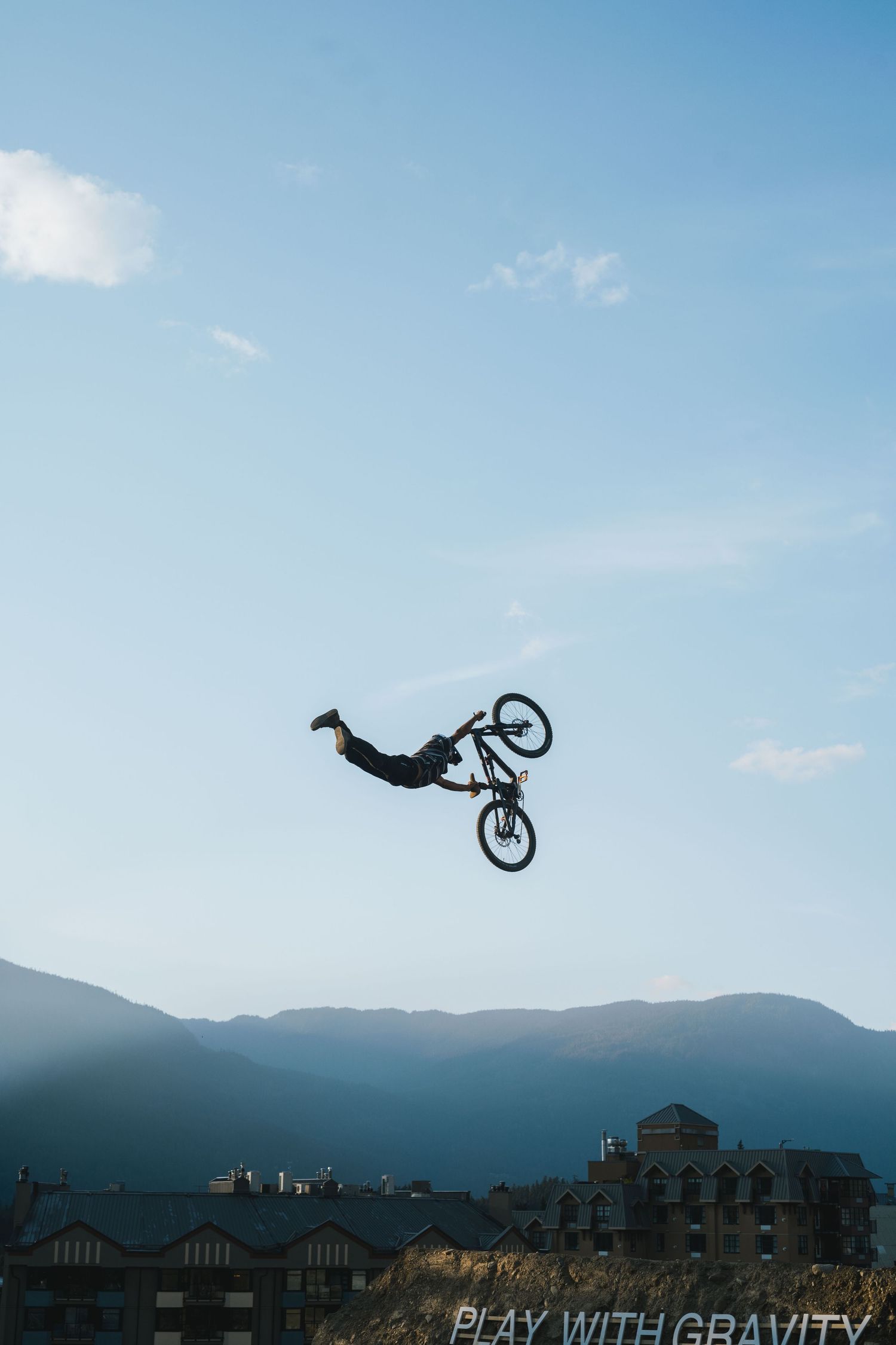 Extreme BMX rider performing a dramatic backflip trick high above mountain town rooftops.