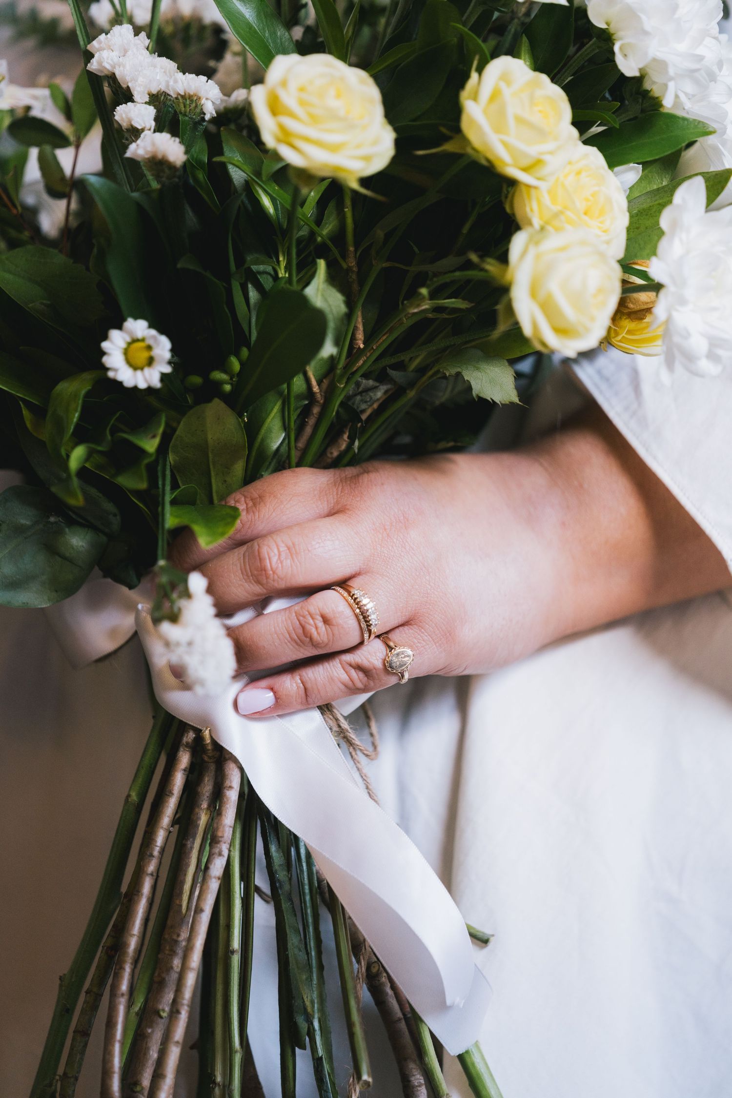 Bride holding white and yellow rose wedding bouquet with gold diamond ring on finger.