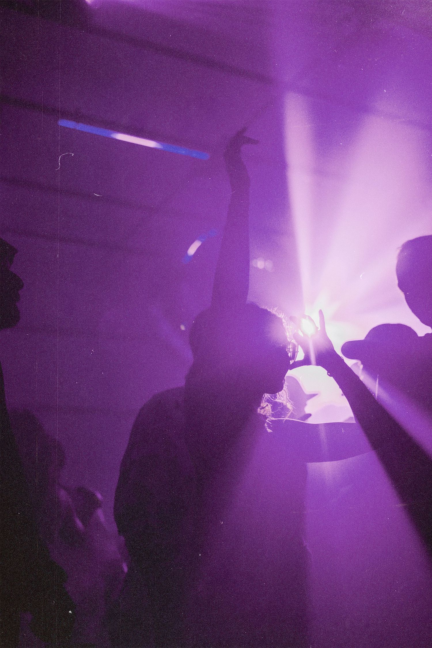 Silhouettes of people dancing with raised hands under purple stage lights at a concert.