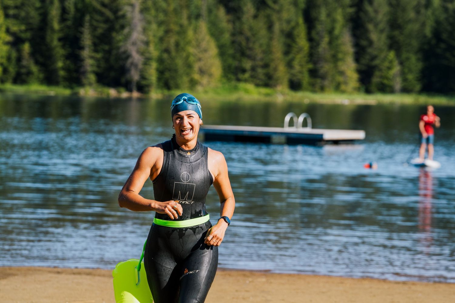 Smiling triathlete in wetsuit running out of a lake during a summer triathlon race.