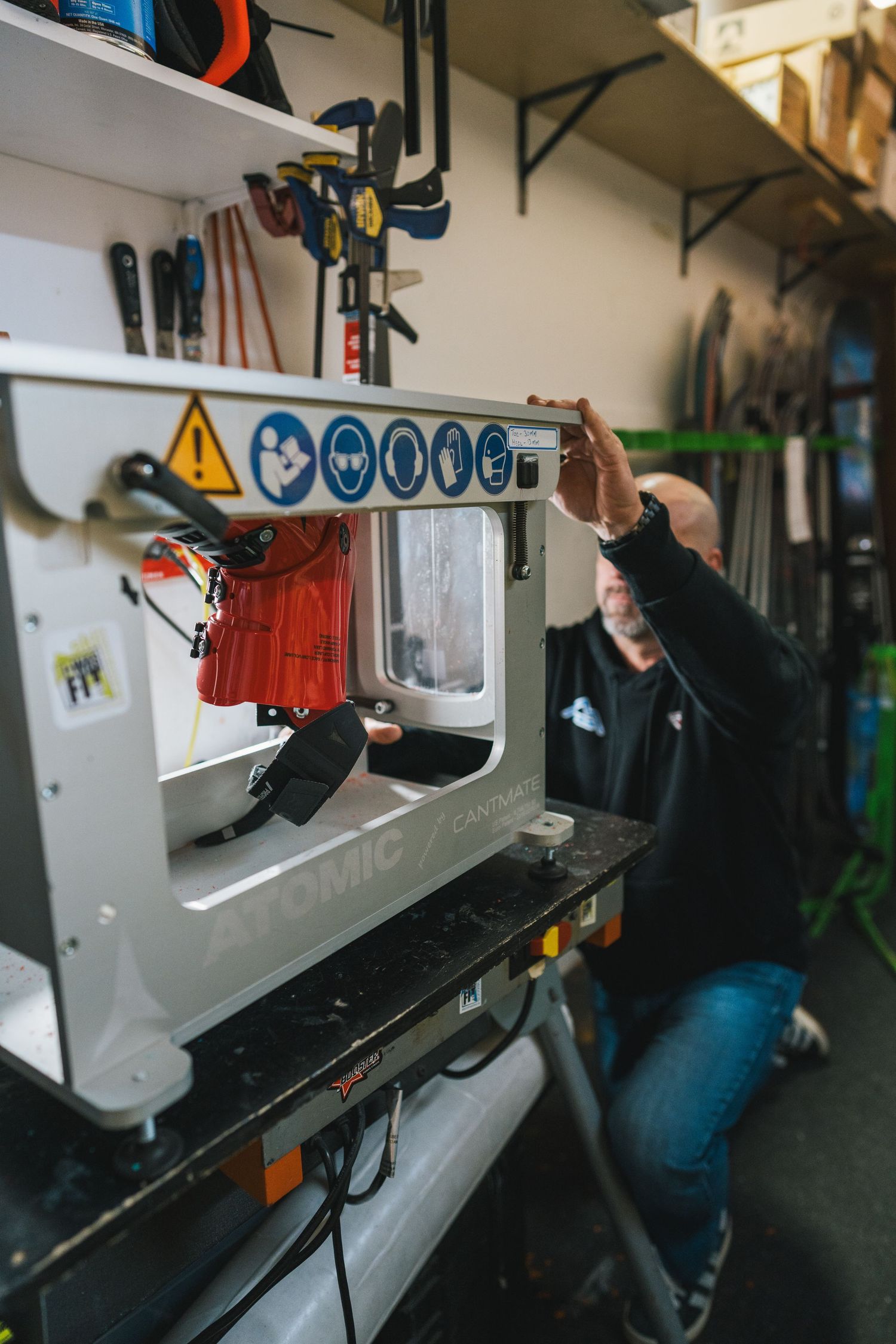 Technician operating an Atomic ski tuning machine in a ski repair workshop.