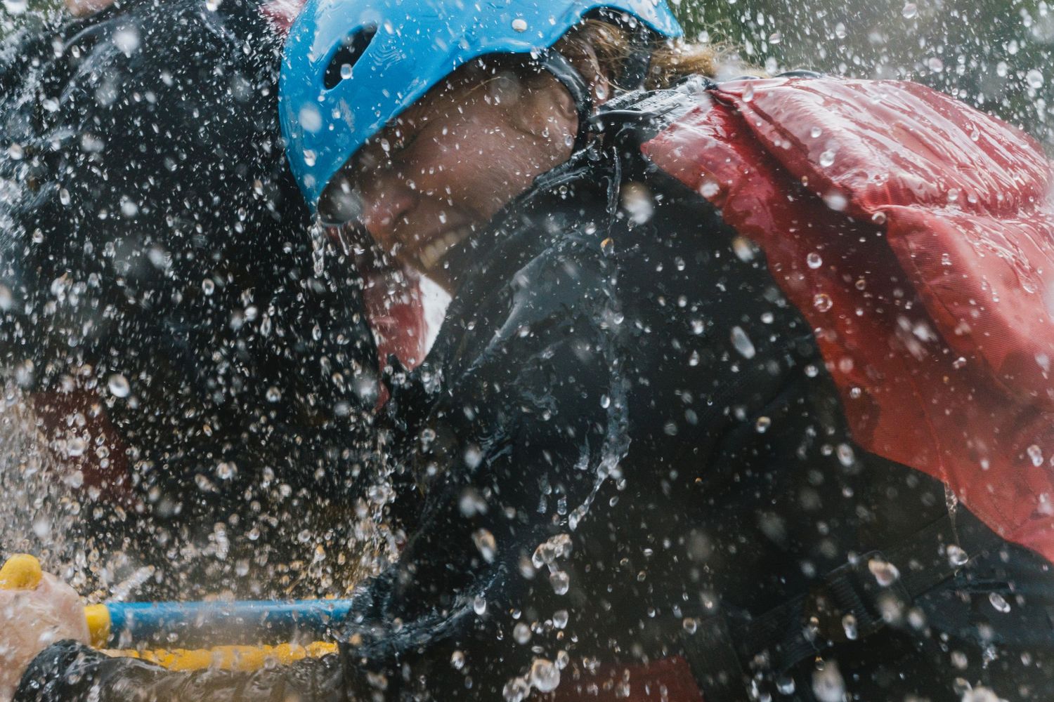 Person white water rafting wearing a blue helmet gets splashed by rushing water during an exciting river adventure.