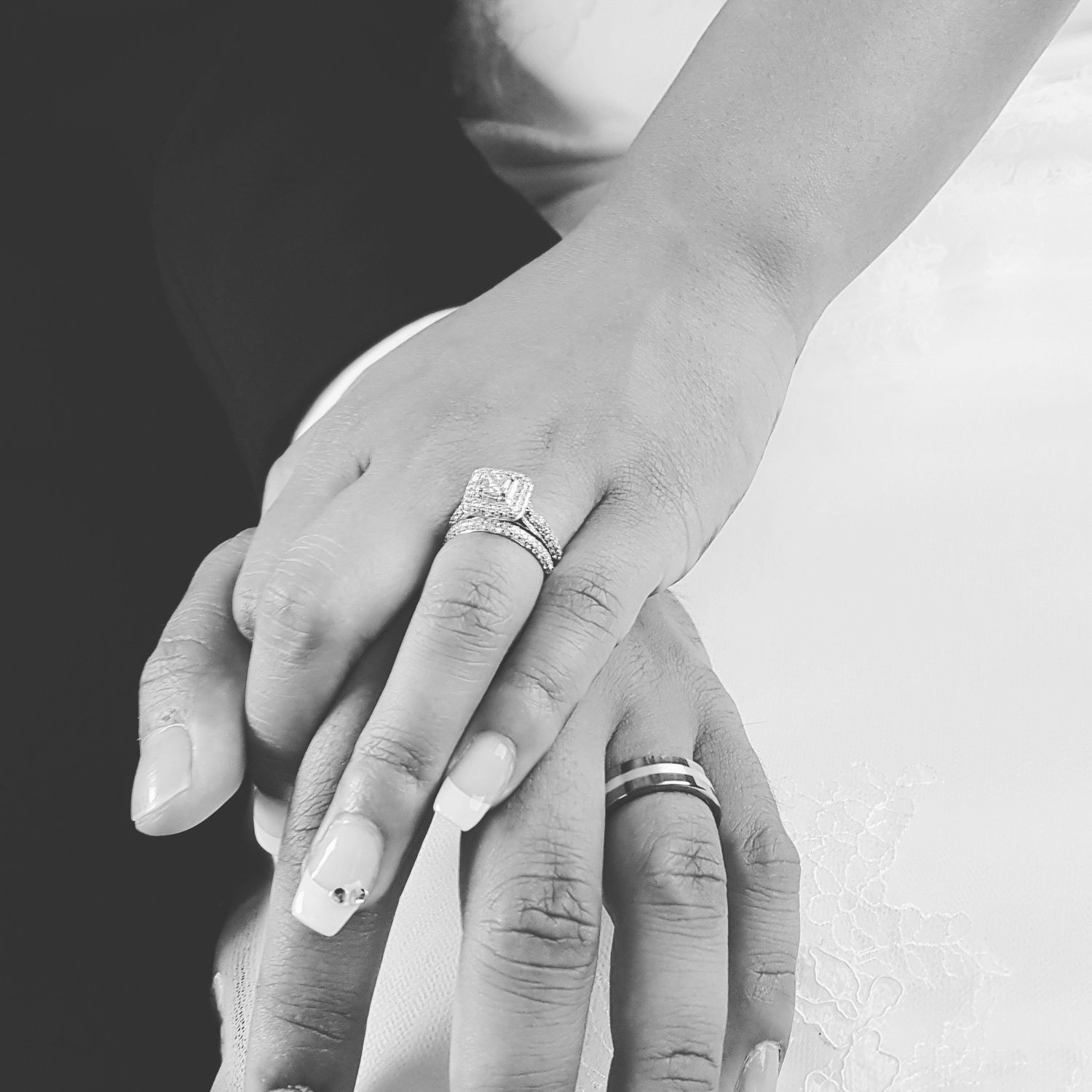 Black and white close-up of hands wearing wedding rings against a dark background.