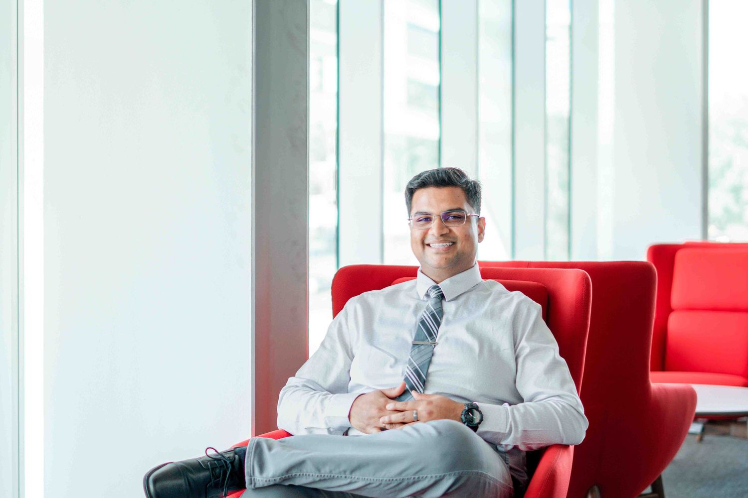 Business professional relaxing in red chair by large office windows.