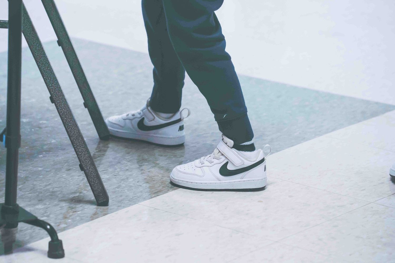 Multiple pairs of sneakers and shoes shown from ankle down on gray floor.