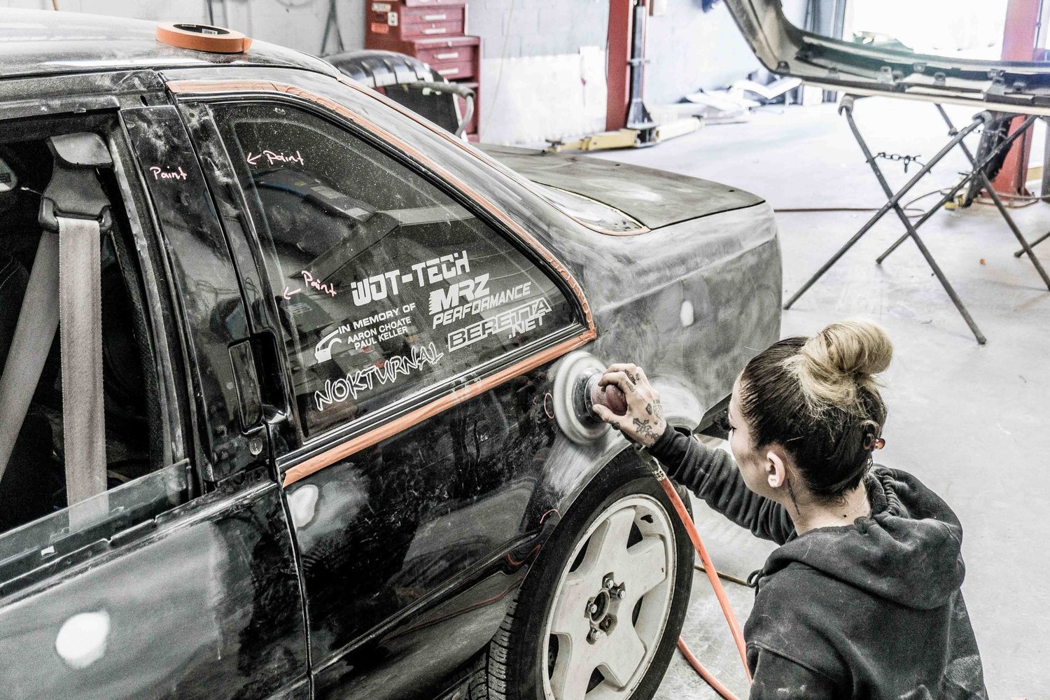 Person detailing a black car with professional equipment in an auto shop.