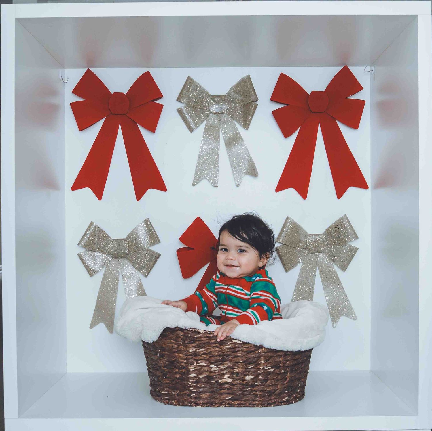 Christmas themed photo setup with red and silver bows against white background and woven basket.