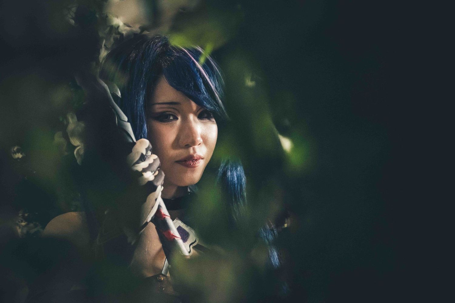 Artistic portrait through leaves showing person with dark hair in natural lighting.