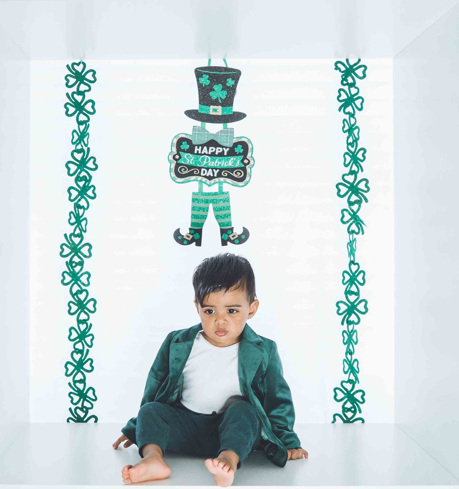 Child in green jacket poses with St Patrick's Day themed decorations and shamrock patterns.