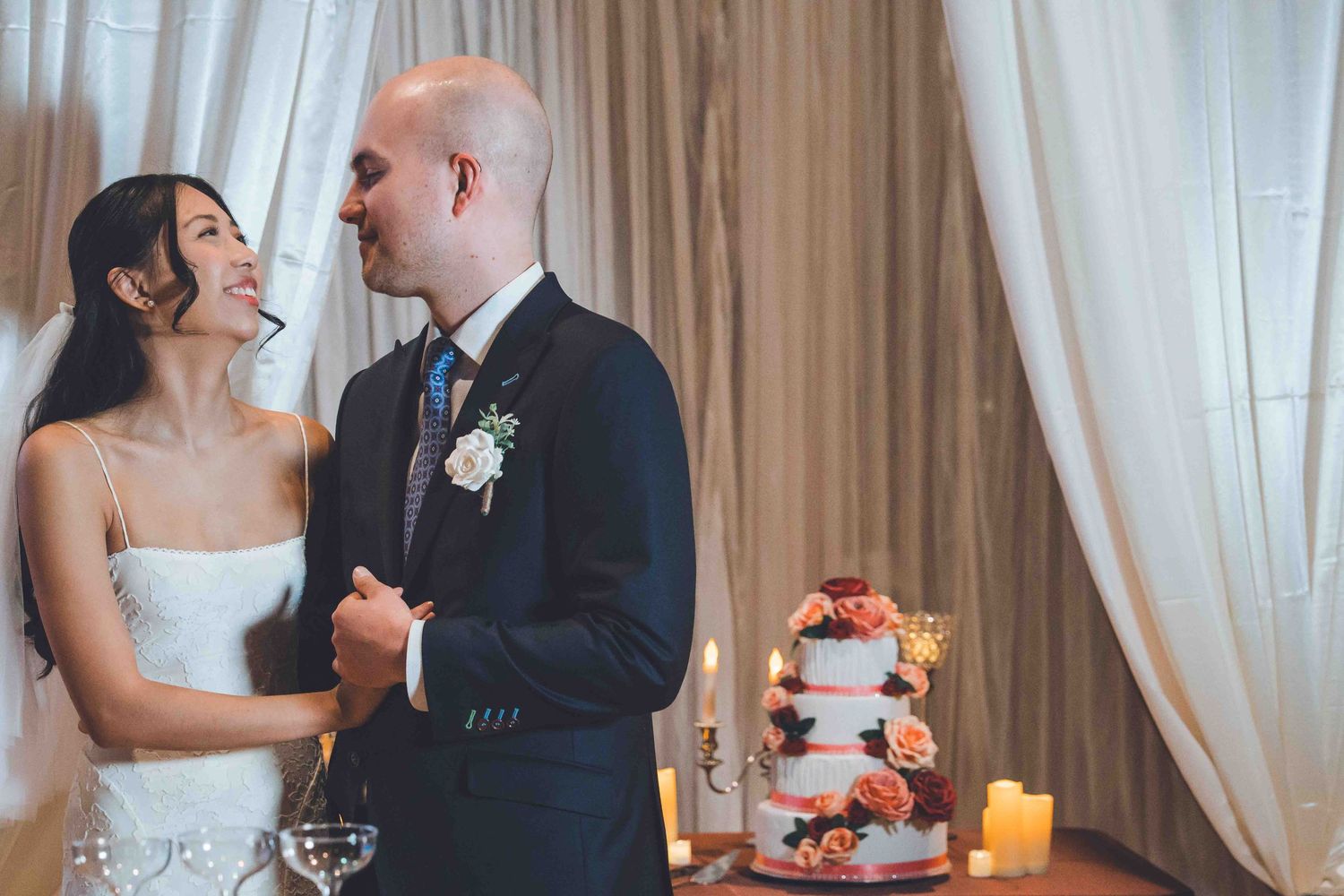 Elegant wedding reception scene with white curtains, candles and table settings in a romantic indoor venue.