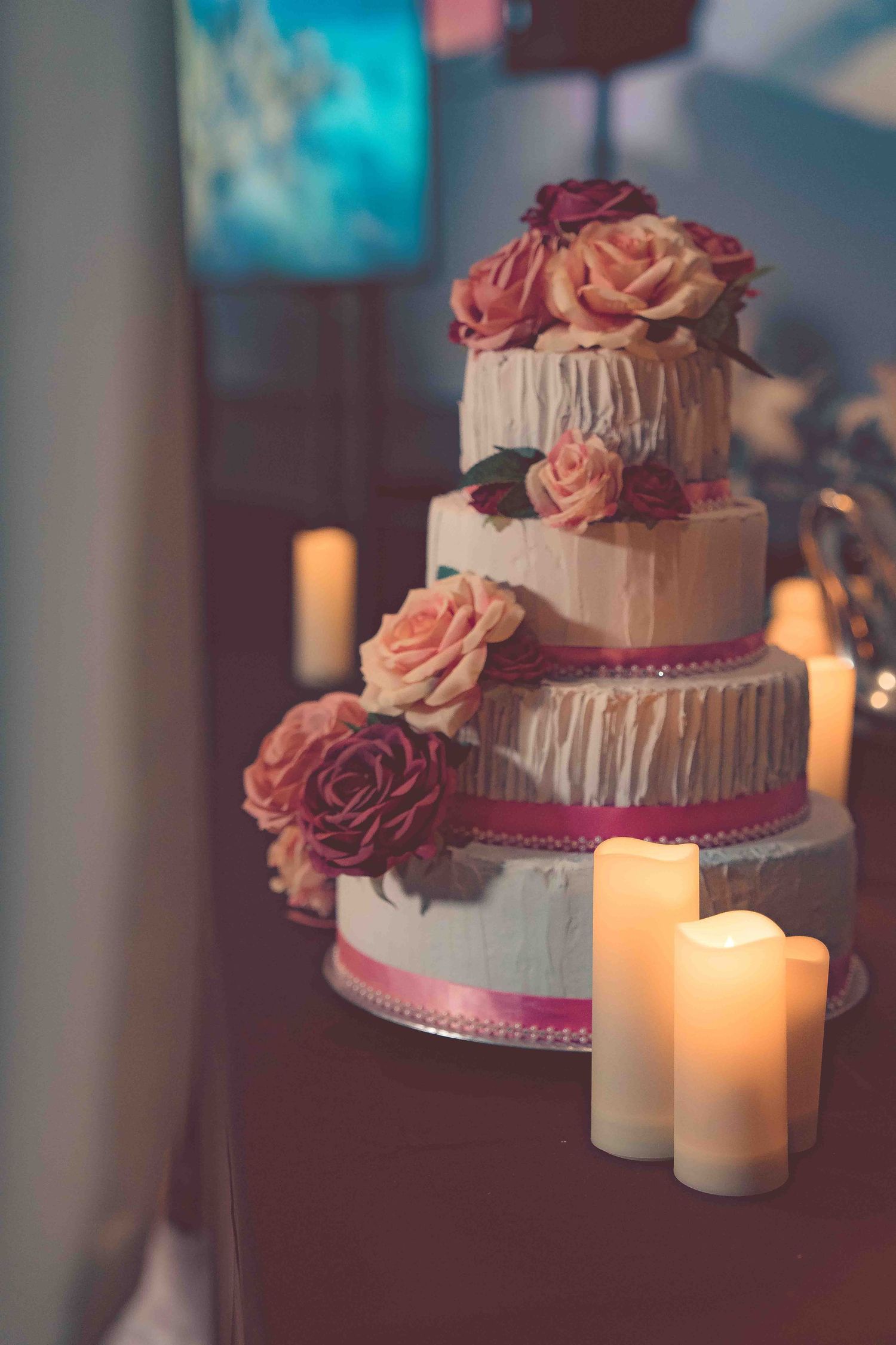 Elegant tiered wedding cake decorated with pink roses and lit candles creating a romantic ambiance.
