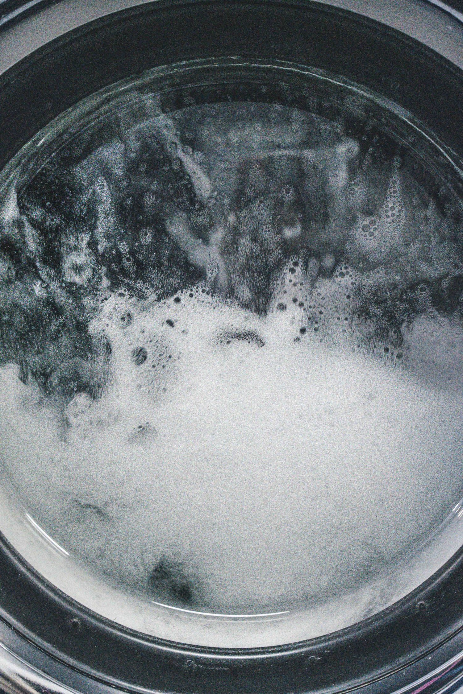 Close-up view of a washing machine drum filled with soapy white foam and water during a wash cycle.