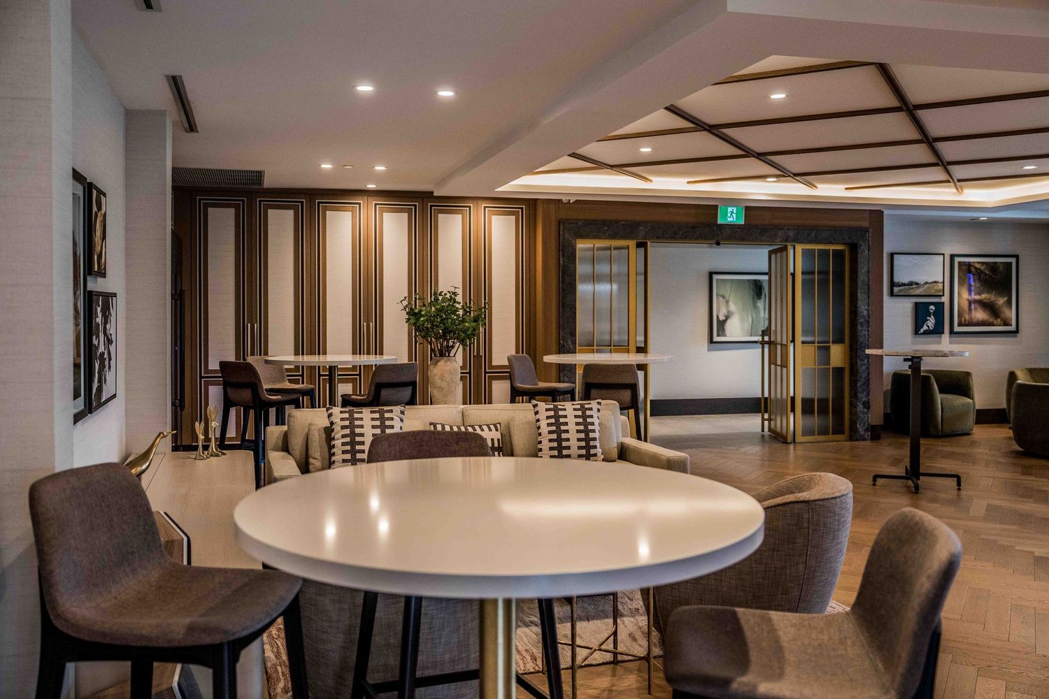 Modern hotel lounge with round white table, gray chairs, warm lighting, and elegant wood-paneled walls in a spacious dining area.