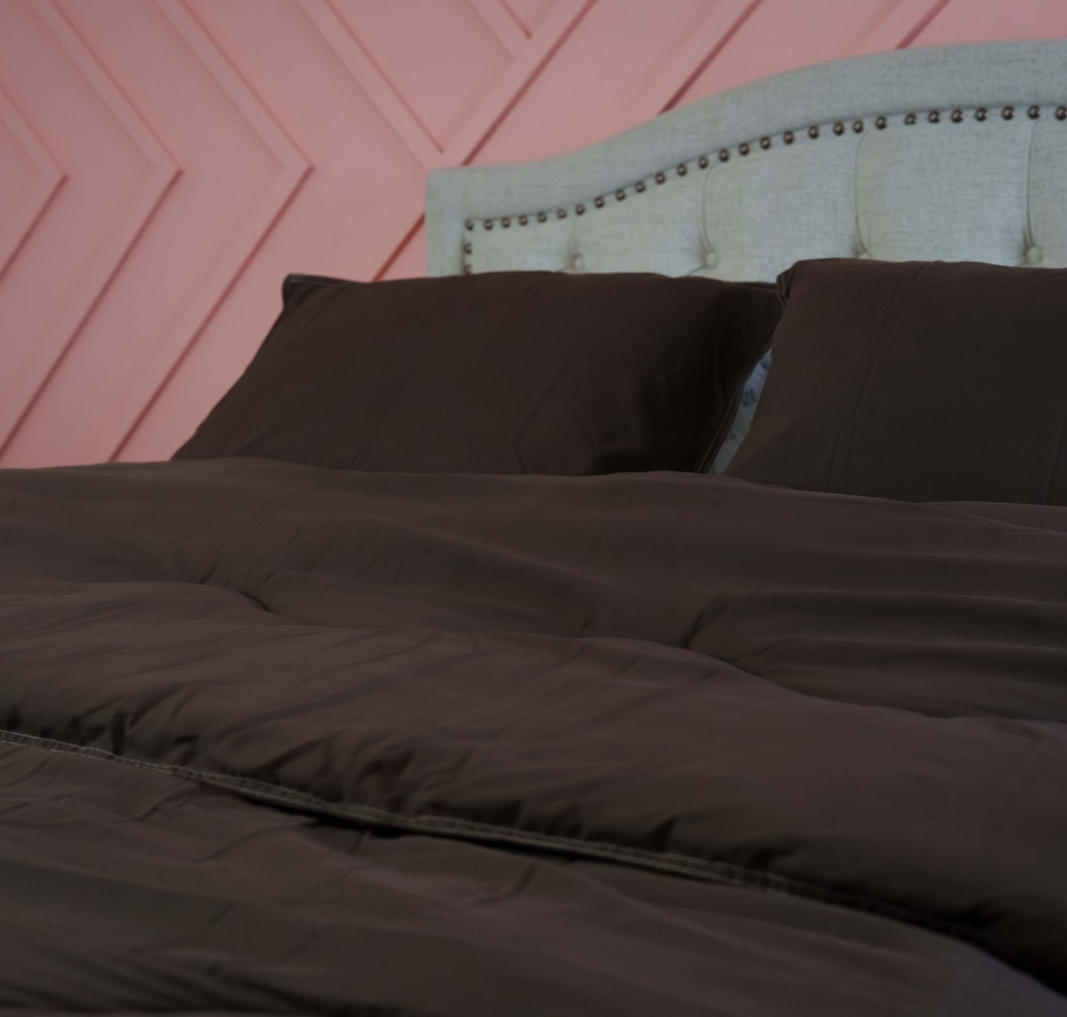 Dark chocolate brown duvet cover and pillow shams on a bed with an upholstered headboard against a pink wall.
