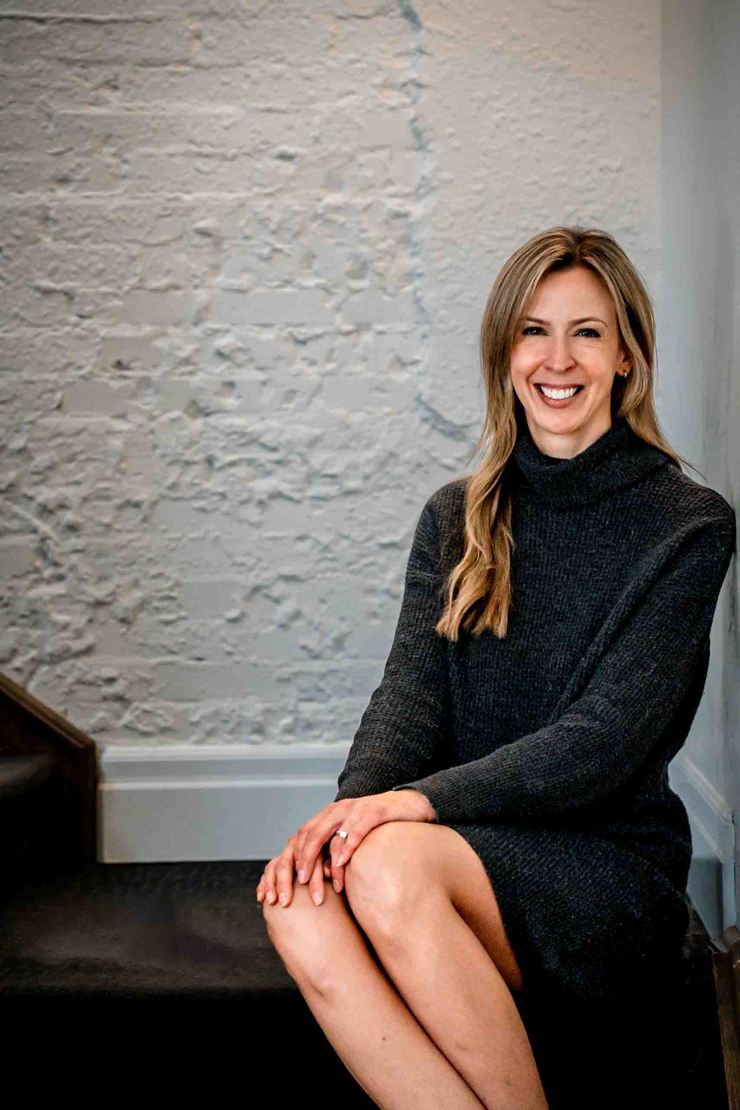 Portrait of someone wearing a cozy black turtleneck sweater against a white wall.