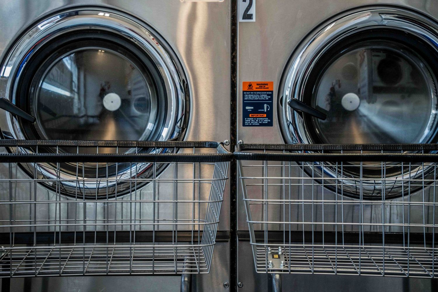 Two stacked commercial washing machines with wire laundry carts in a modern laundromat.