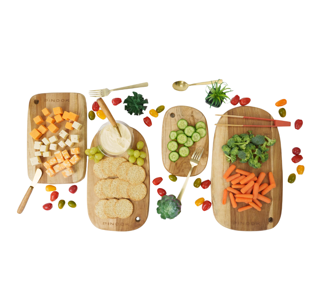 Four rectangular bamboo serving boards topped with colorful fresh vegetables and cheese.
