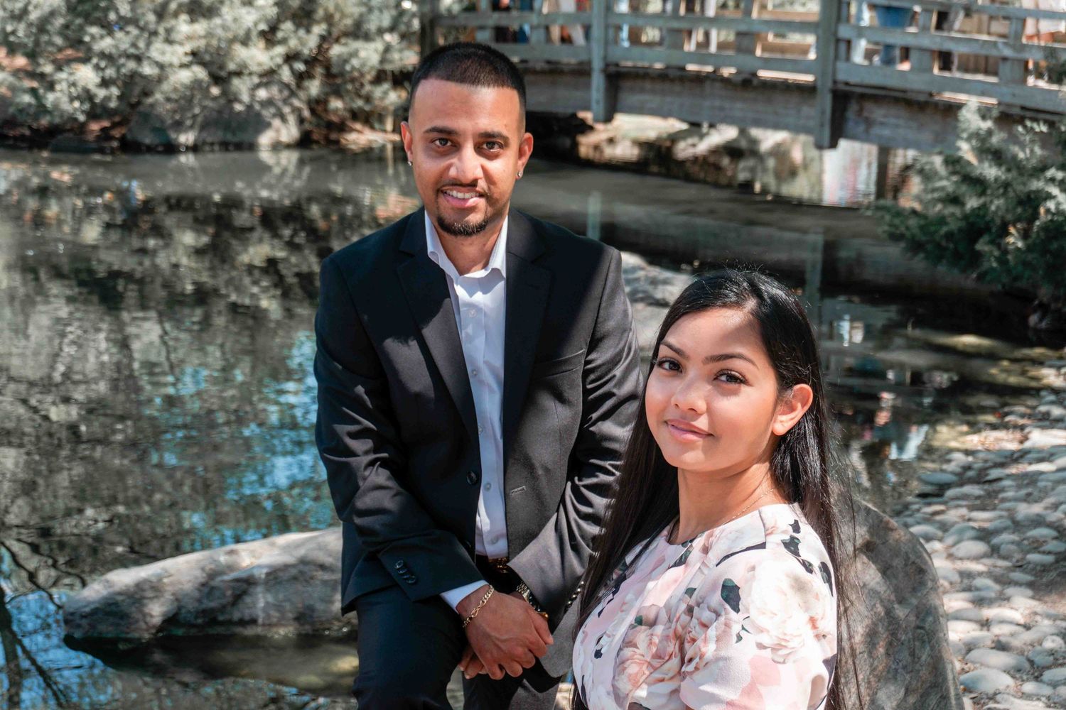 A couple poses together on stone steps surrounded by cherry blossoms and greenery.