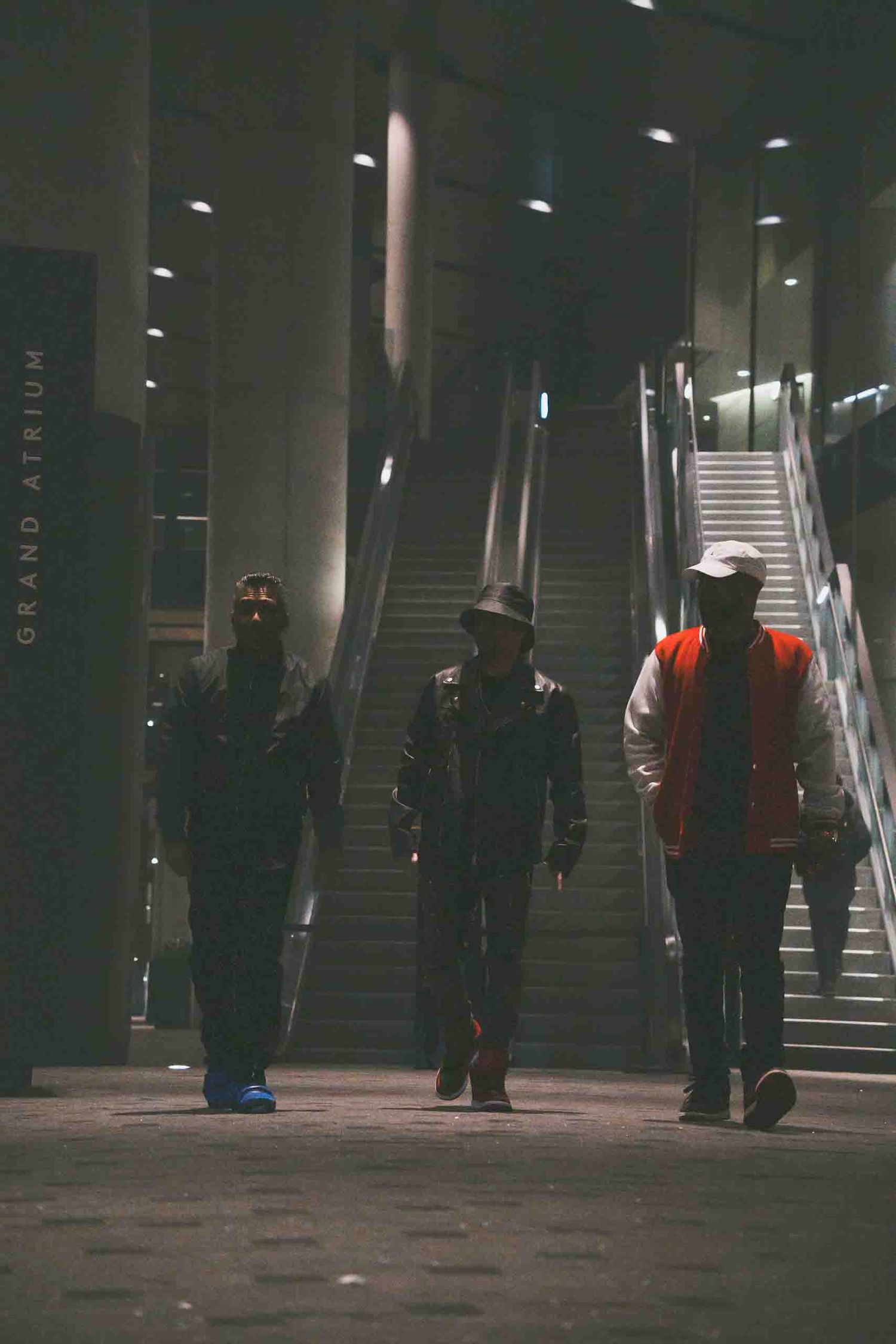 Three people walking up illuminated stairs in a dark urban setting.