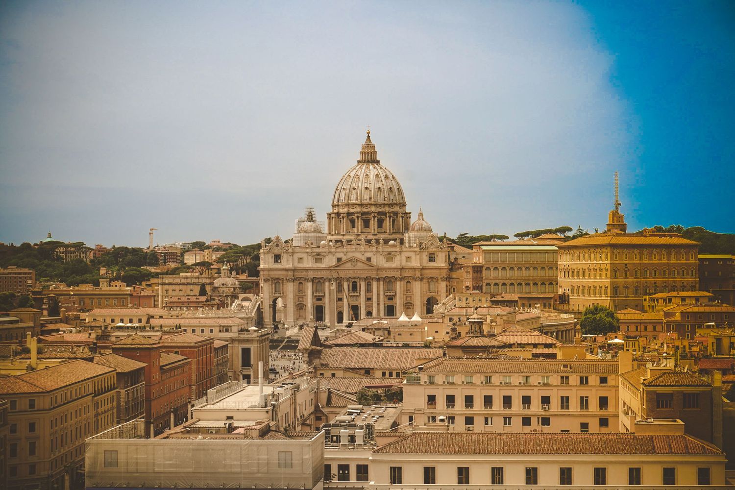 Panoramic skyline view of St. Peter's Basilica and Vatican City buildings under bright blue sky.