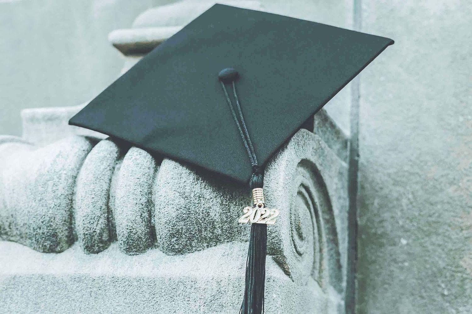 Graduation mortarboard cap resting on stone architectural detail in muted tones.