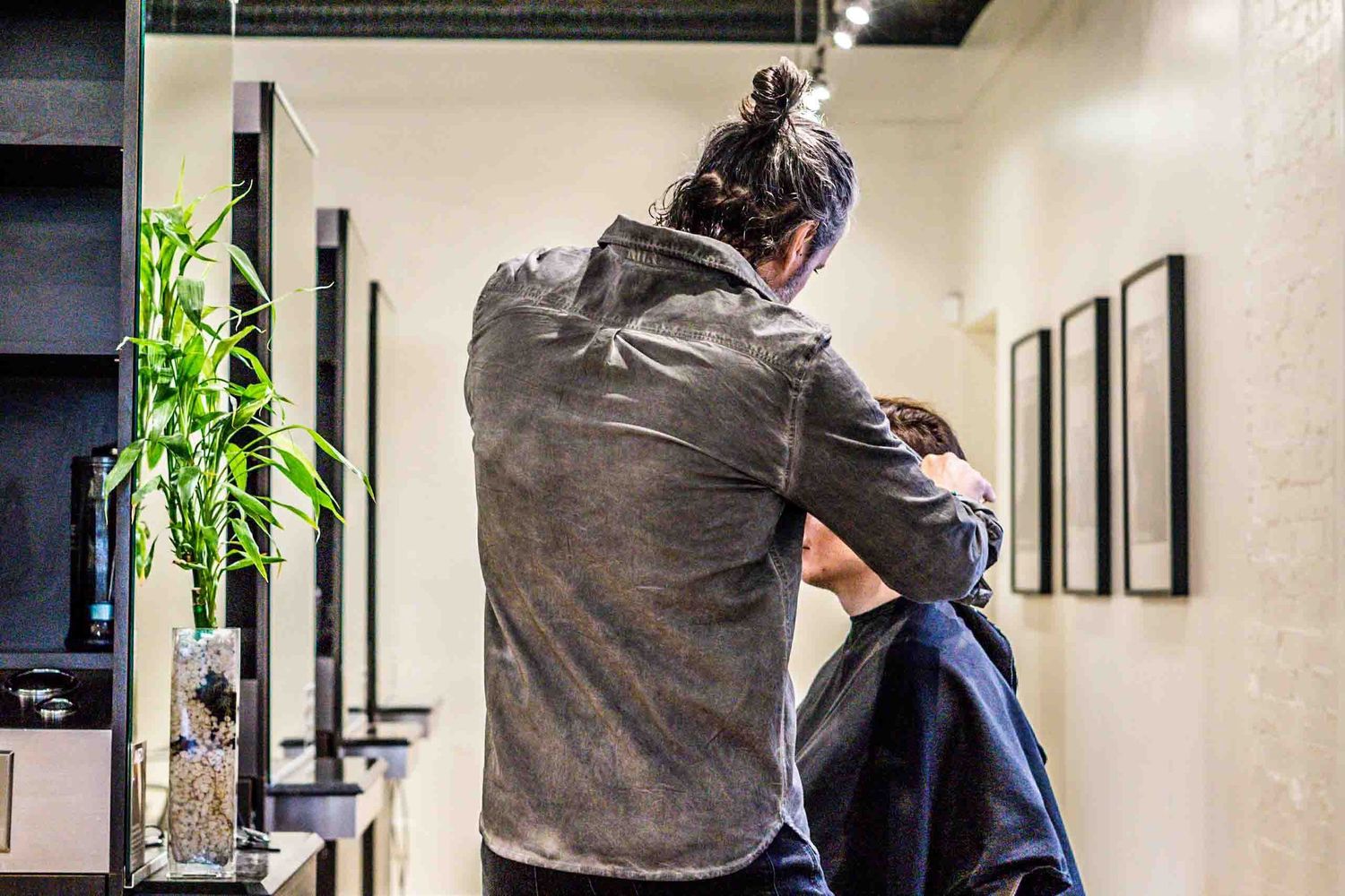 A hairstylist in dark clothing works on styling a client's hair in a salon setting.