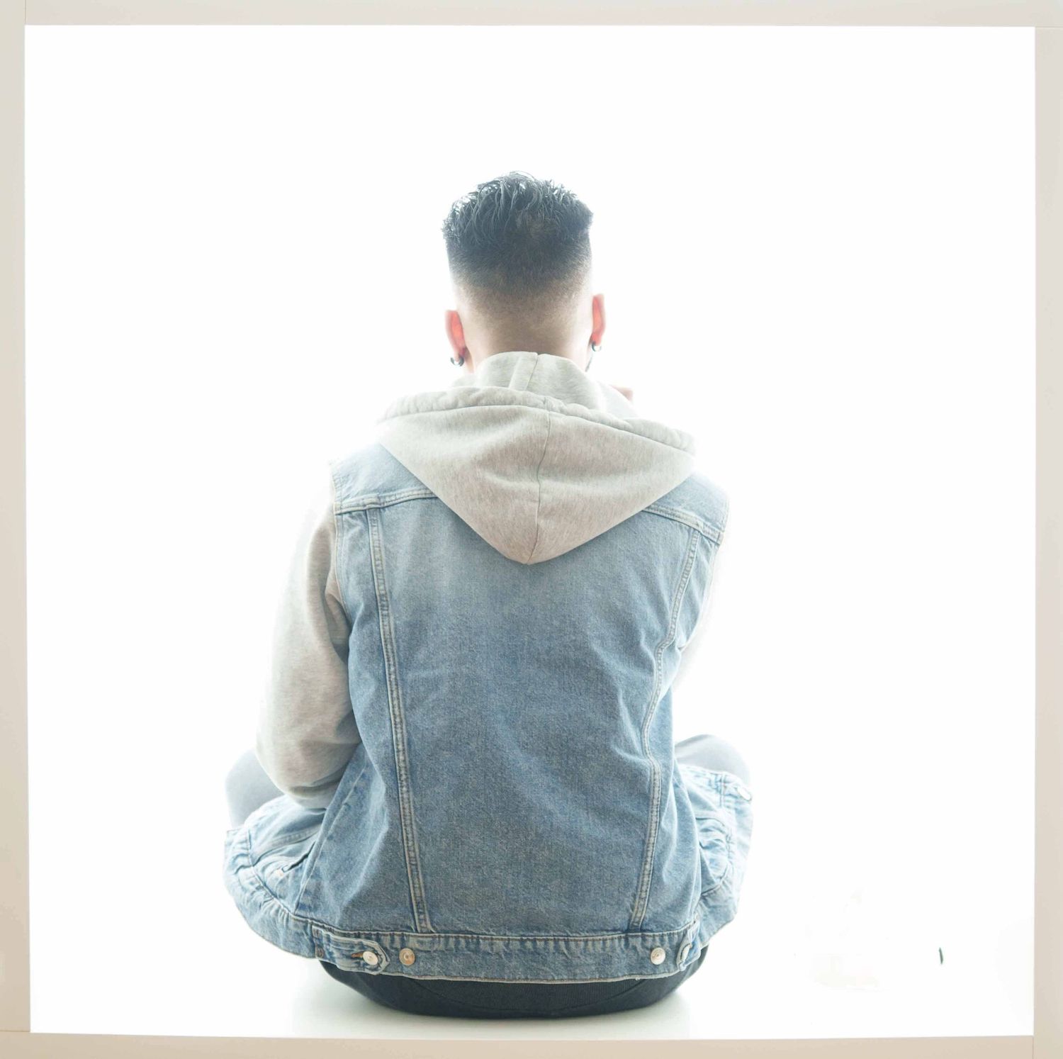 Back view of someone sitting in denim jacket against white background.