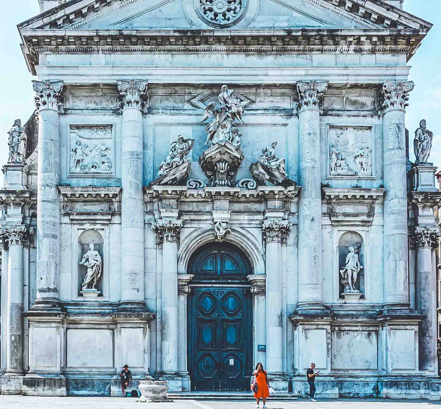 Ornate baroque church facade with blue doors and classical architectural details in pale stone.