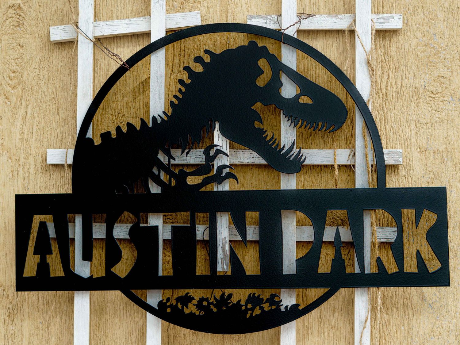 Black metal sign featuring Jurassic Park-style dinosaur silhouette with text reading 'Austin Park'.