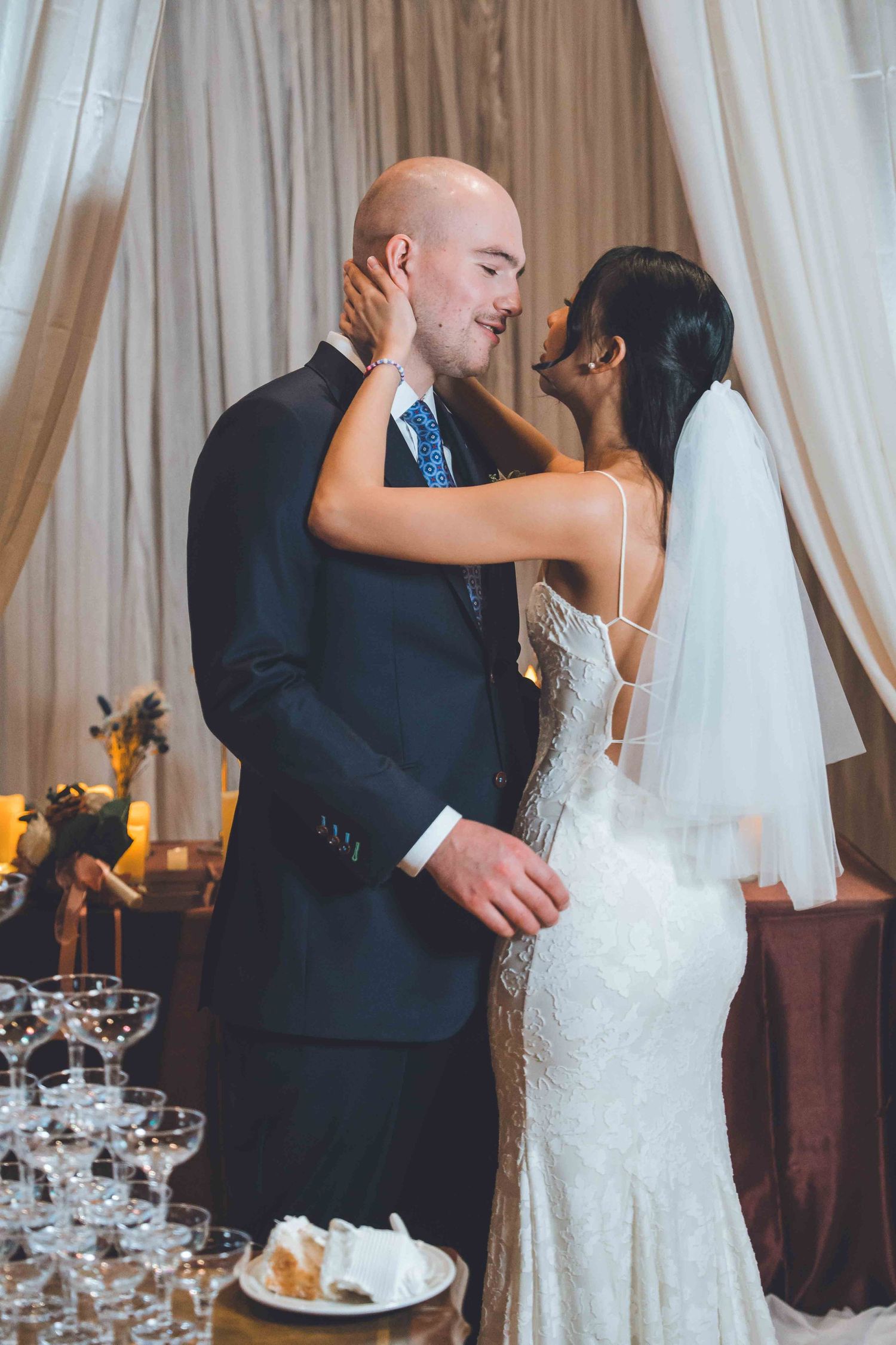 Romantic wedding moment as newlyweds share an intimate kiss by a champagne tower.