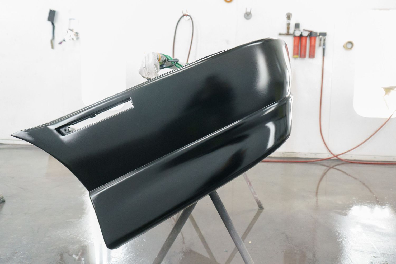 Freshly painted black automotive body panel on a stand in a professional paint booth.