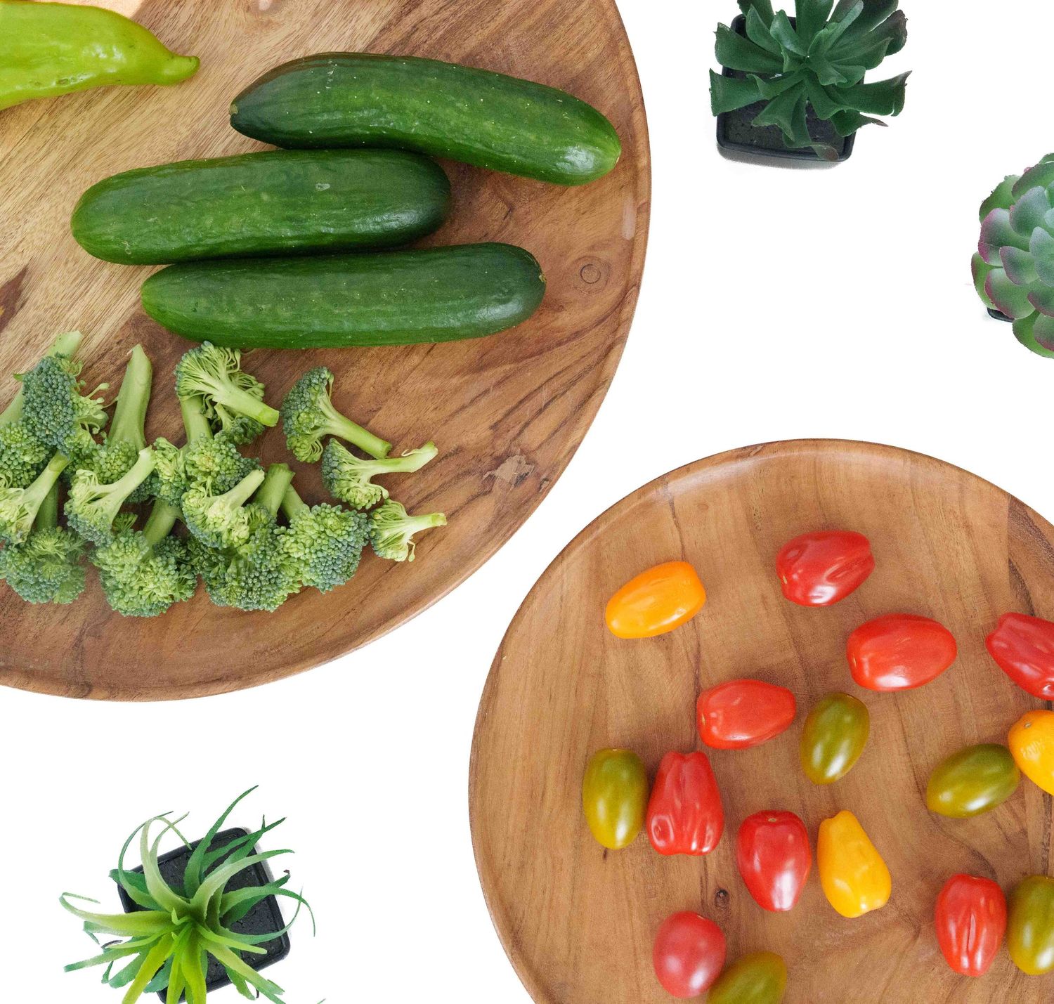 Round wooden boards displaying fresh cucumbers, broccoli, and colorful cherry tomatoes.