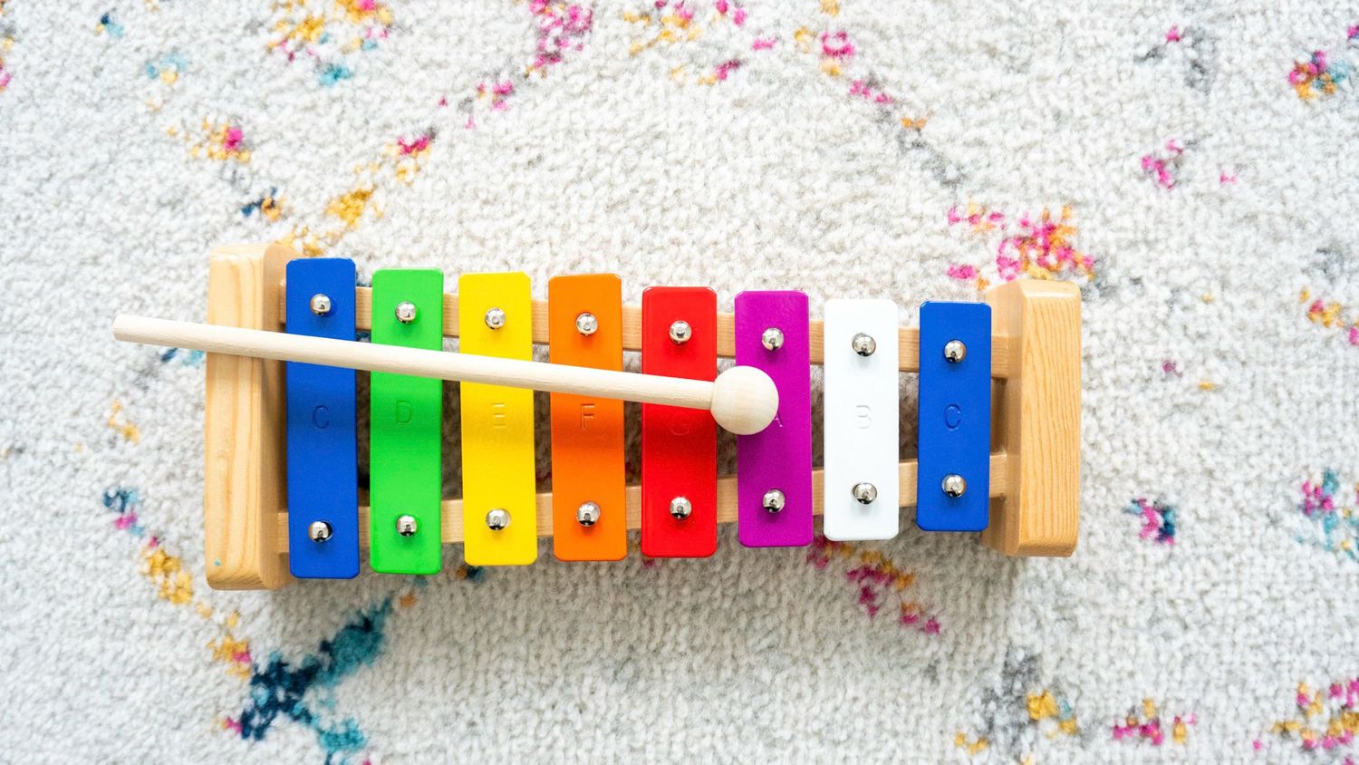 Colorful xylophone with rainbow keys on a white speckled background.