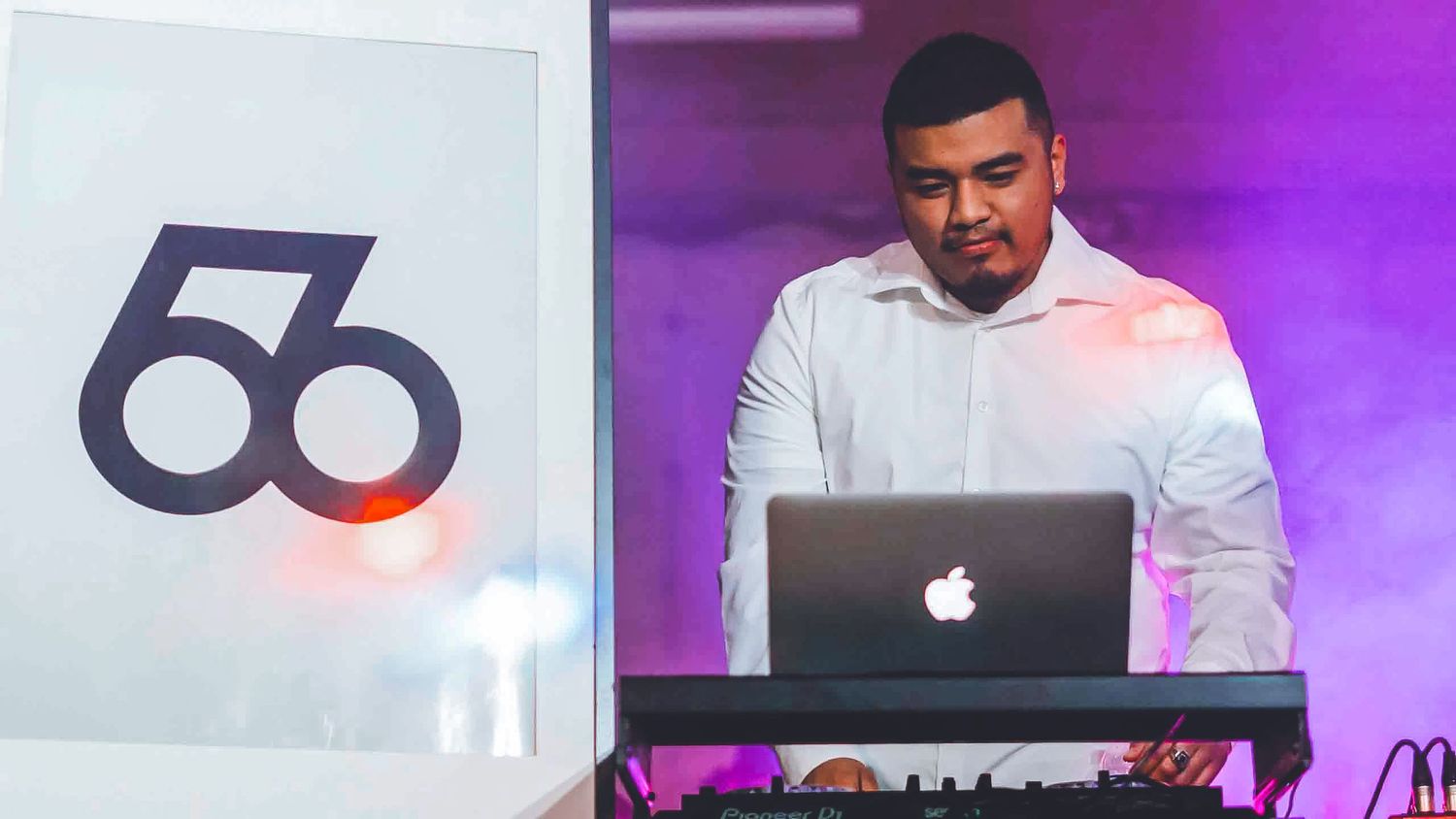 DJ setup with purple lighting and Apple MacBook visible on stage.