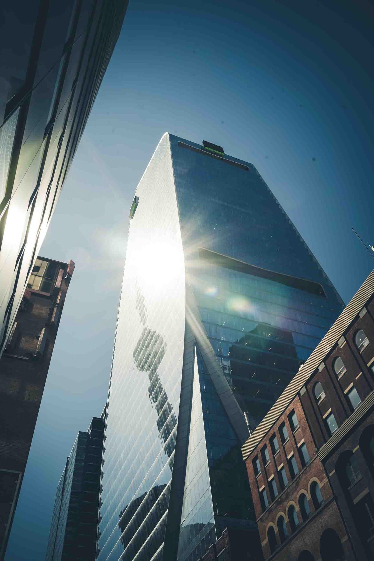 Modern glass skyscraper photographed from below against bright blue sky.
