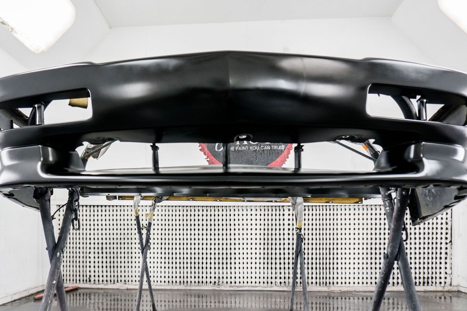Black car front bumper primed and ready for painting in an auto body paint booth.