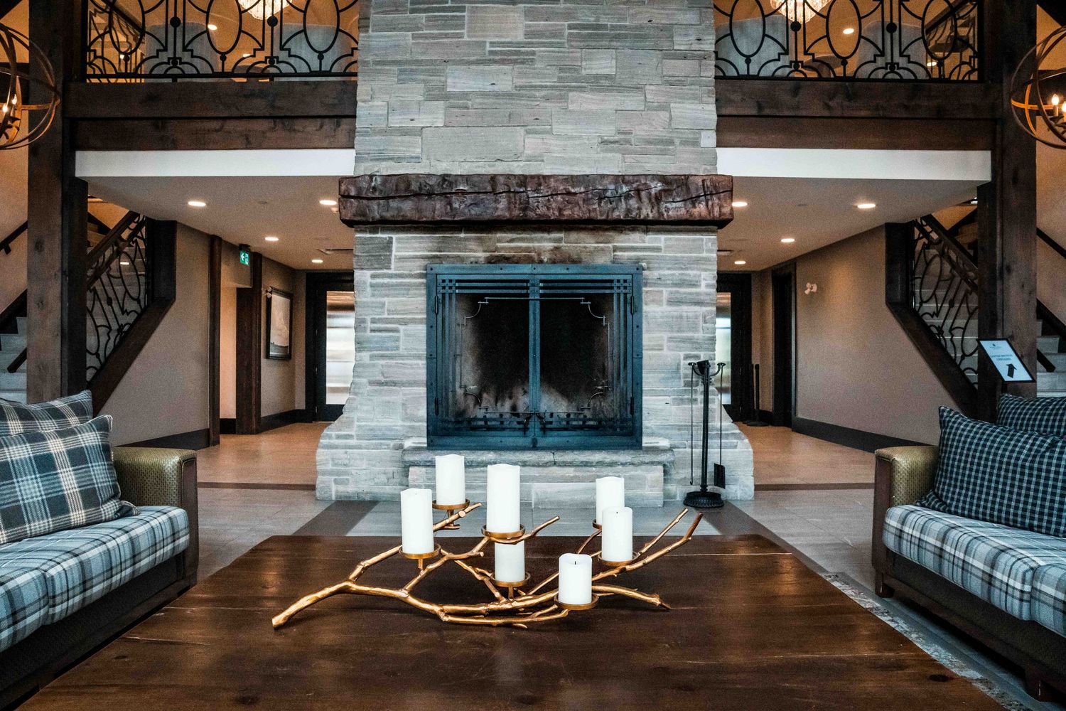 Elegant lodge lobby featuring a stone fireplace, wooden coffee table with candles, and plaid sofas on hardwood floors.