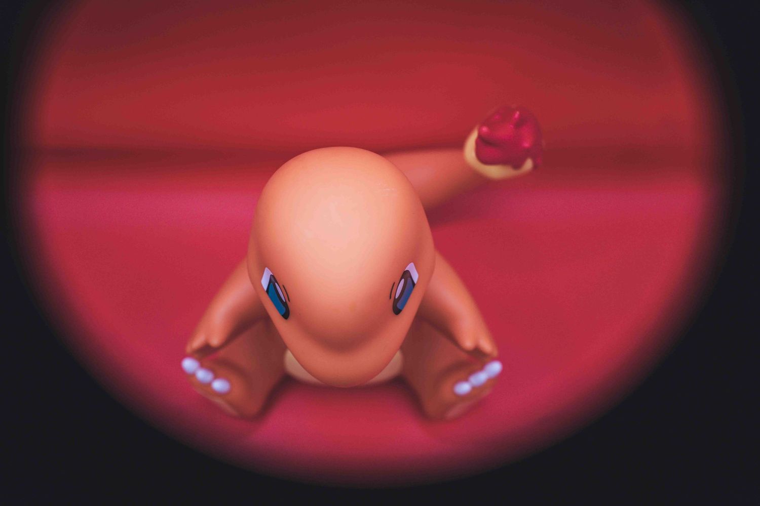 Charmander Pokemon figure viewed through a circular vignette on a red background.