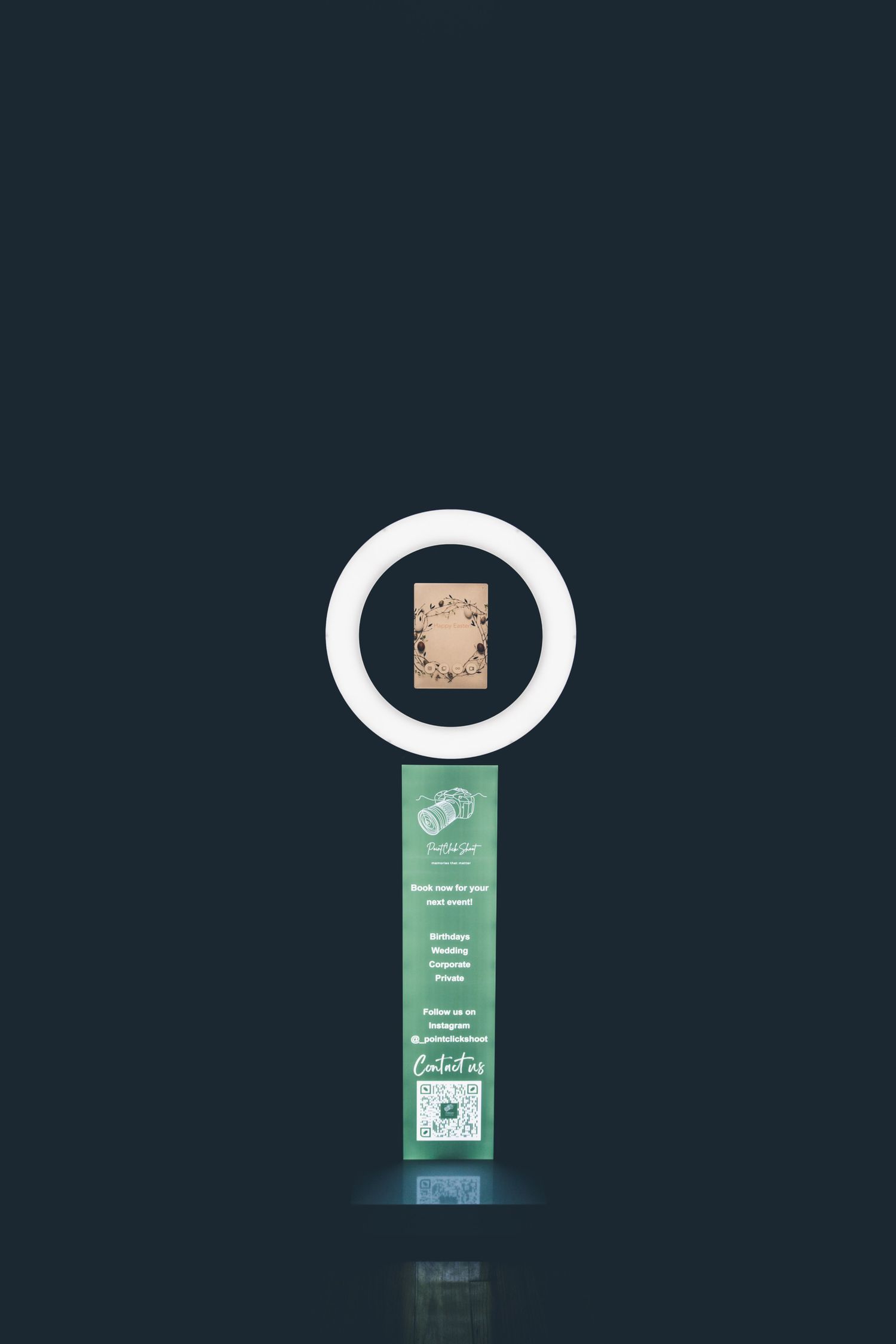Minimalist photo booth display with glowing ring light against dark background.