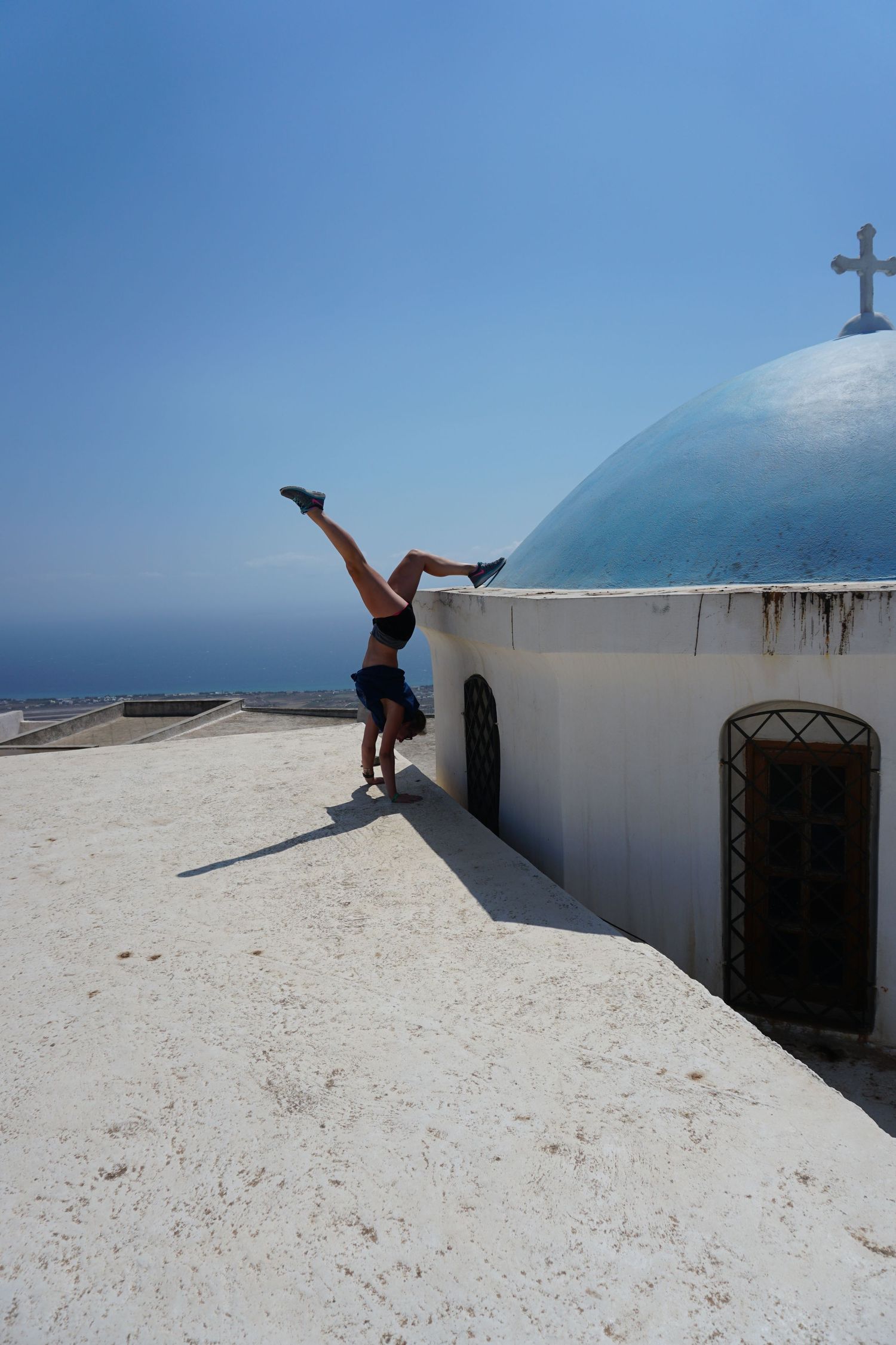 Person performs parkour moves on white Mediterranean-style building rooftops against blue sky.