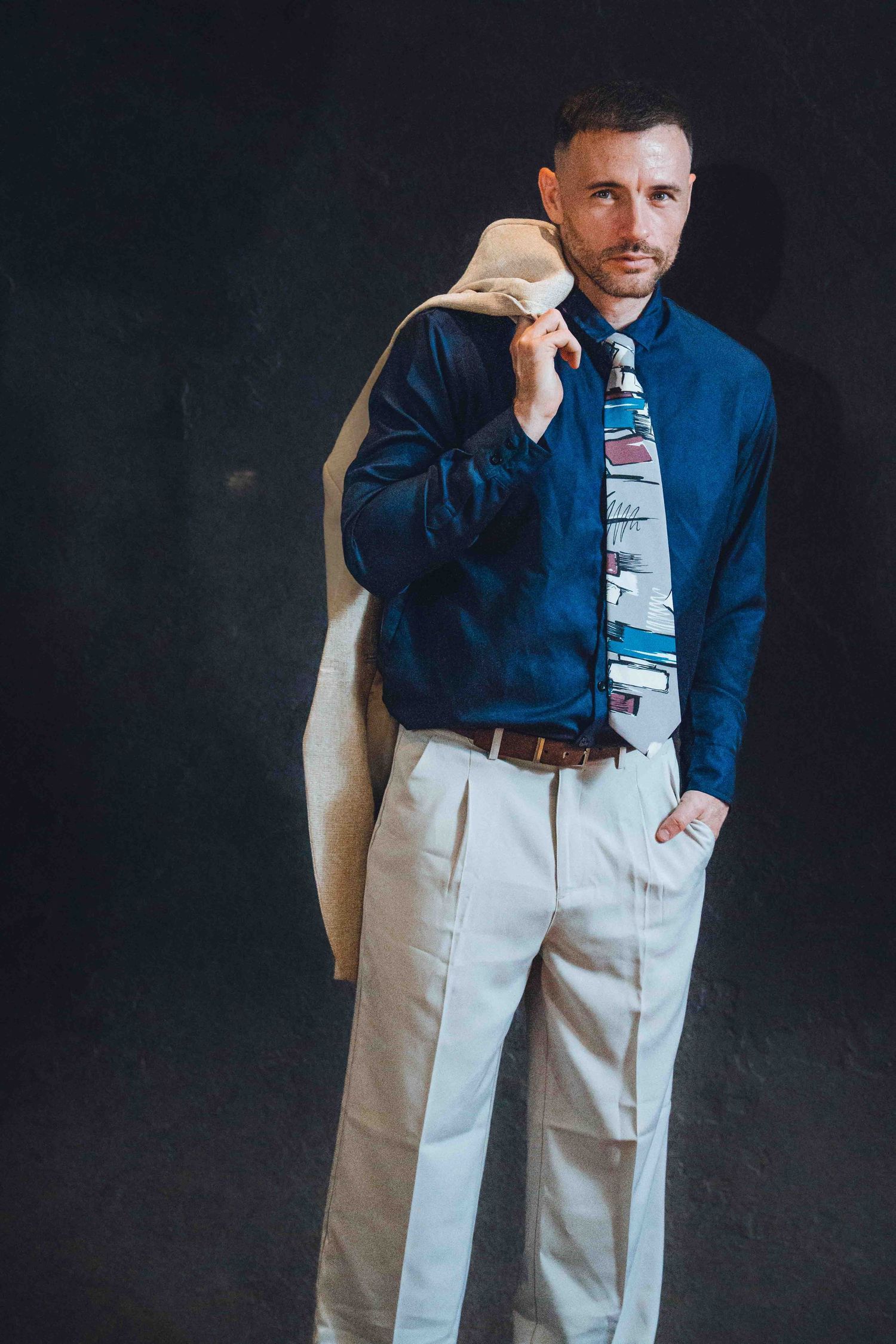Man wearing navy blue shirt and white pants in multiple poses against dark background.